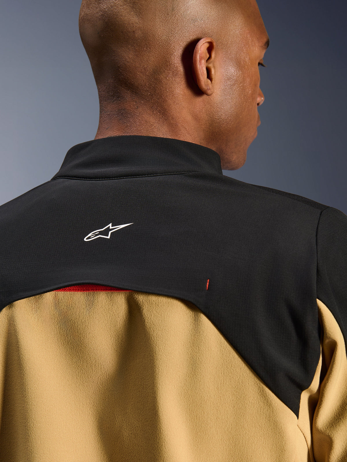 Chaqueta Alpinestars Provoke, chaqueta urbana de motociclismo, negro y camel, primer plano de la parte superior de la espalda y la zona del cuello con el logotipo blanco de Astars sobre un canesú negro y paneles inferiores color camel, diseño técnico contemporáneo inspirado en el outdoor