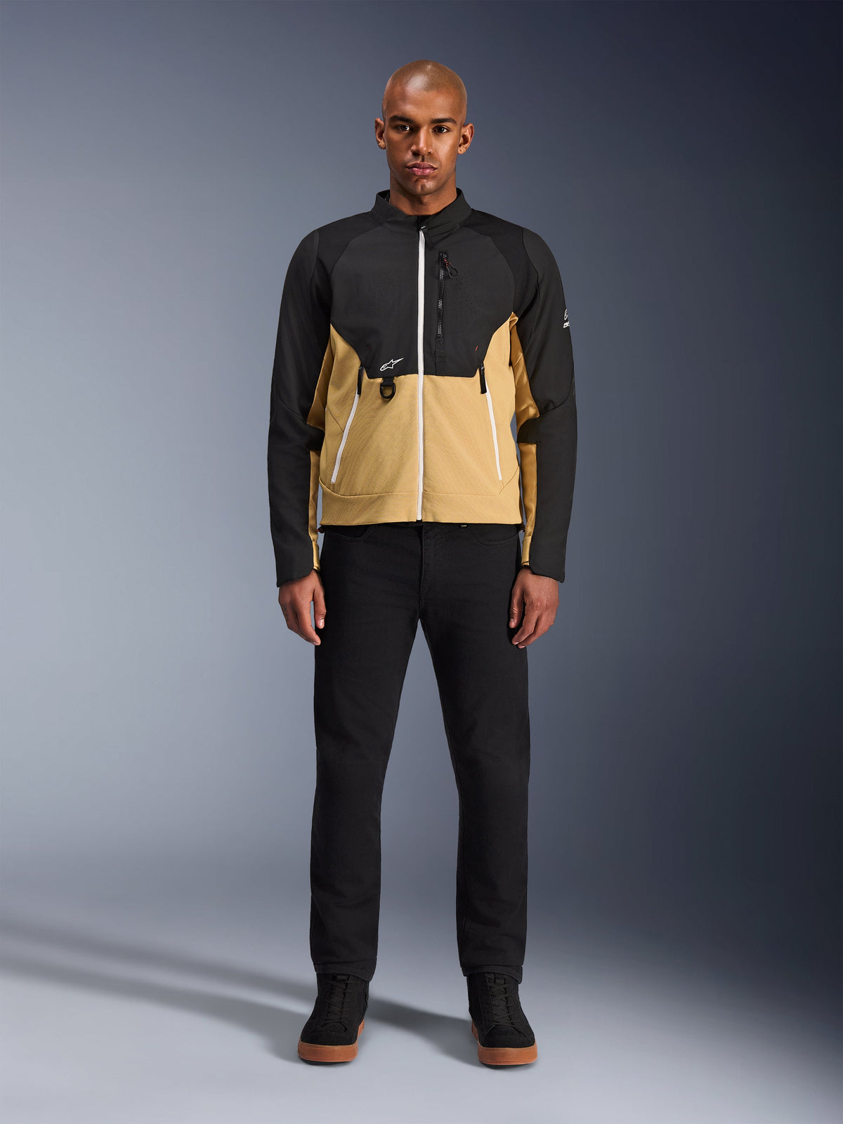 Chaqueta Alpinestars Provoke en Black Camel, chaqueta urbana de motociclismo con diseño bicolor en negro y camel, lucida por un modelo con pantalones y calzado negros, silueta contemporánea con cremalleras blancas y construcción técnica de softshell.