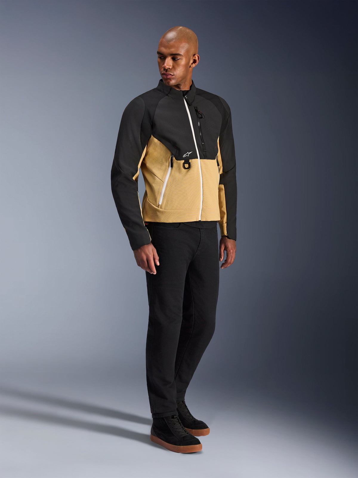 Chaqueta Alpinestars Provoke, chaqueta urbana para motocicleta, Negro Camel, usada por un modelo con pantalones negros y zapatillas, diseño textil bitono con parte superior negra y parte inferior del torso color camel, detalles de cremalleras blancas, equipamiento de conducción urbana contemporáneo