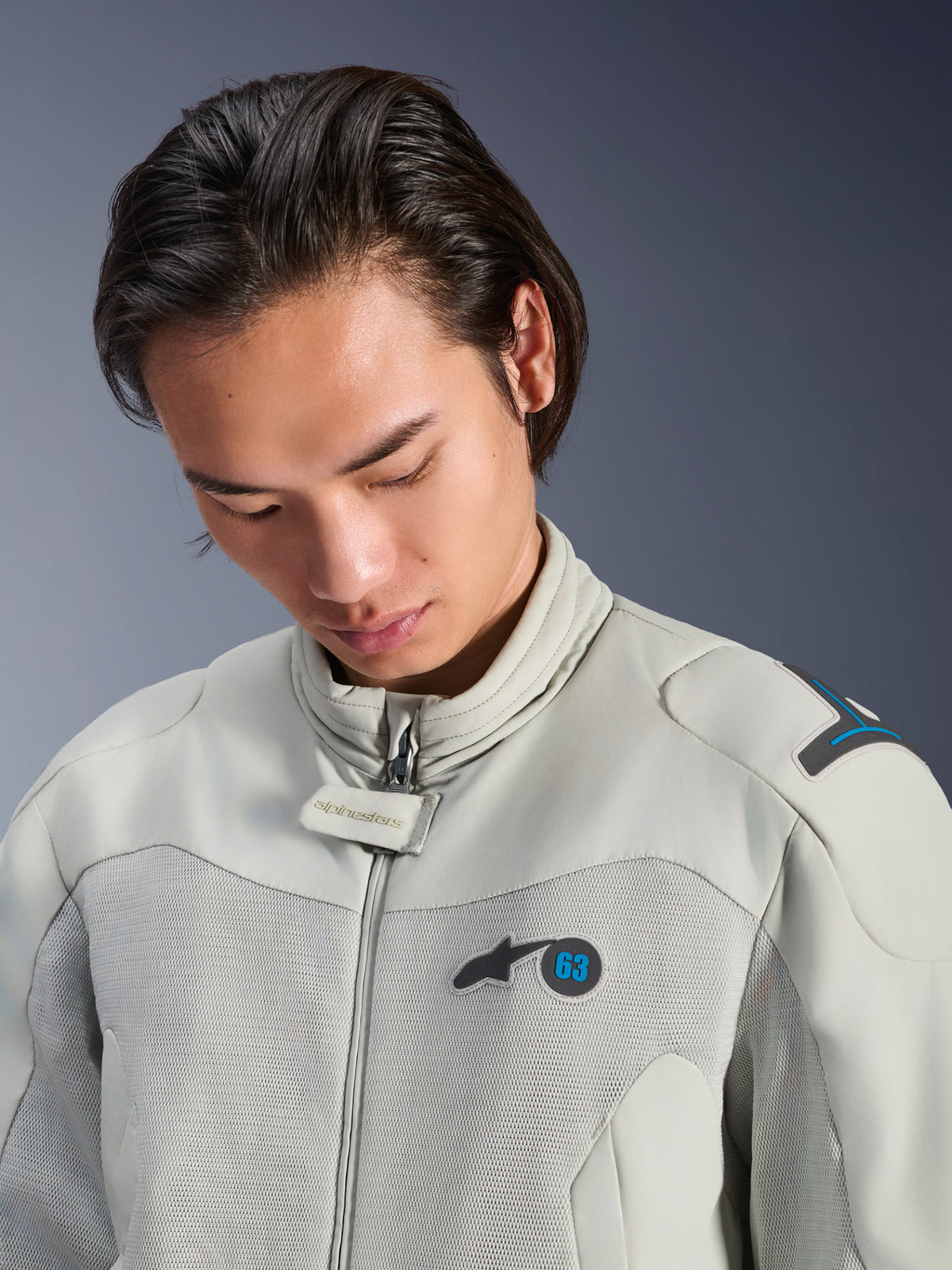 Modelo masculino con la chaqueta Alpinestars Circal-1 Air en color Metal Gray con detalles en Methyl Blue, vista de primer plano que resalta el cuello, los paneles de malla del pecho y el logotipo minimalista, equipamiento de moto urbana sostenible.