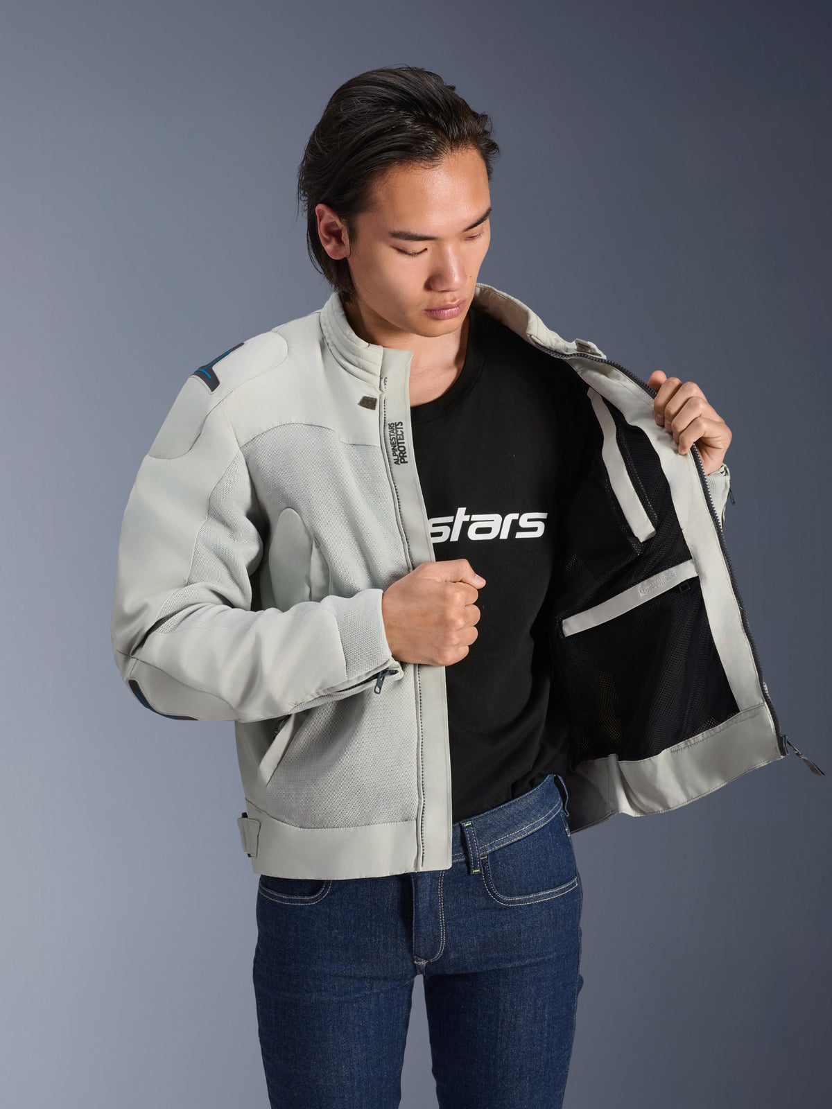 Chaqueta Alpinestars Circal-1 Air, gris metalizado, abierta para mostrar el forro interior de malla y los detalles de los bolsillos, usada por un modelo con camiseta negra con logo y vaqueros azules, estilo de motociclismo urbano