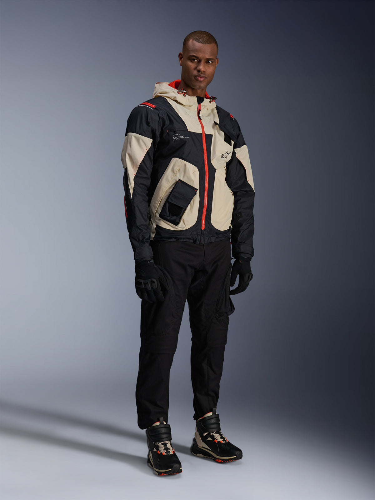 Alpinestars Acteon Pants, Black motorcycle pants, worn with a black, beige, and red Mogress Air Jacket, black riding gloves, and matching high-top riding sneakers, contemporary urban motorcycle gear for men