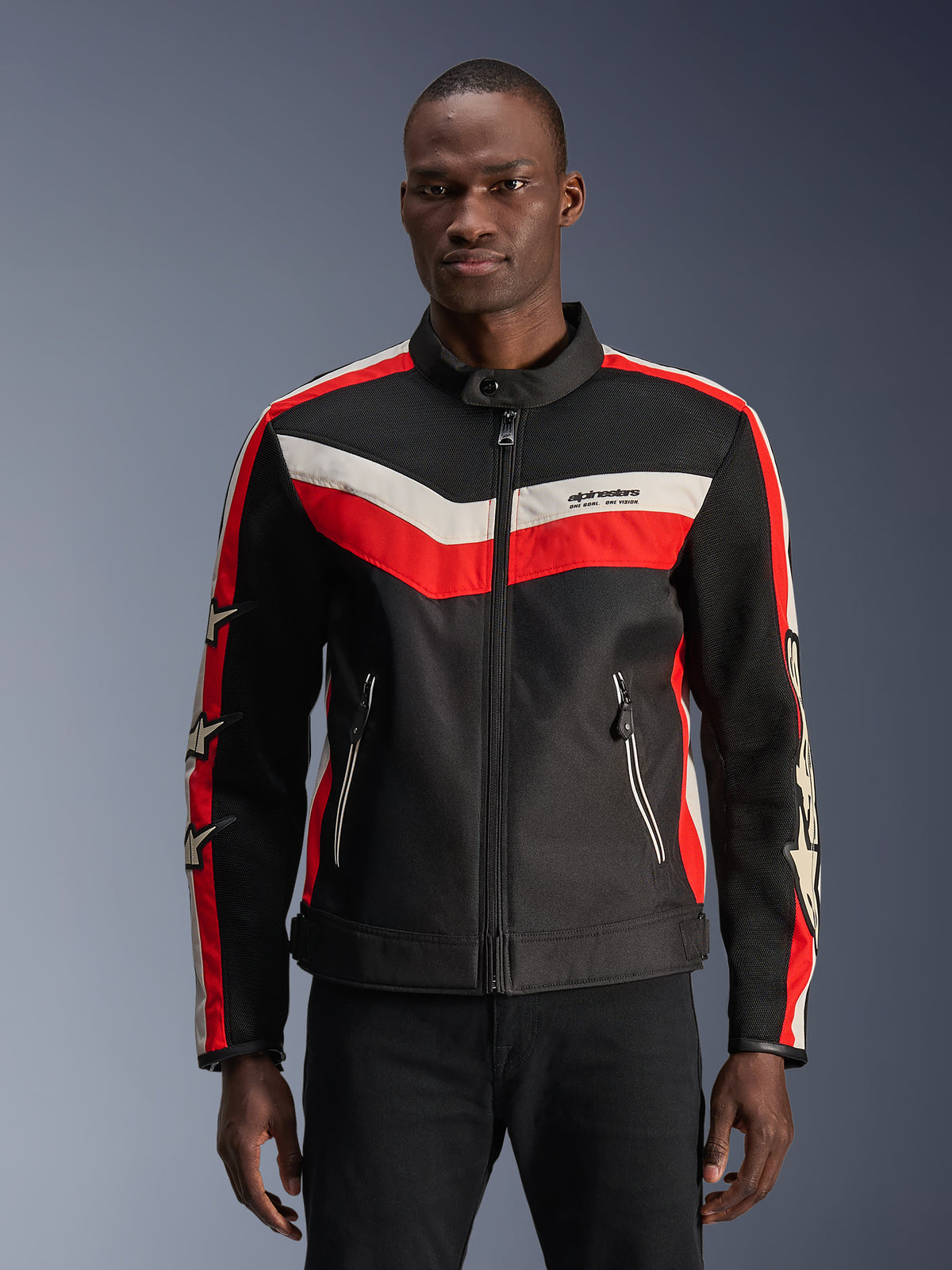 Alpinestars T-Dyno Air Jacket, negra con franjas en chevrón en rojo brillante y crudo, detalles de estrellas en las mangas, cuello alto con cremallera frontal, bolsillos con cremallera, diseño de chaqueta de moto textil de inspiración vintage