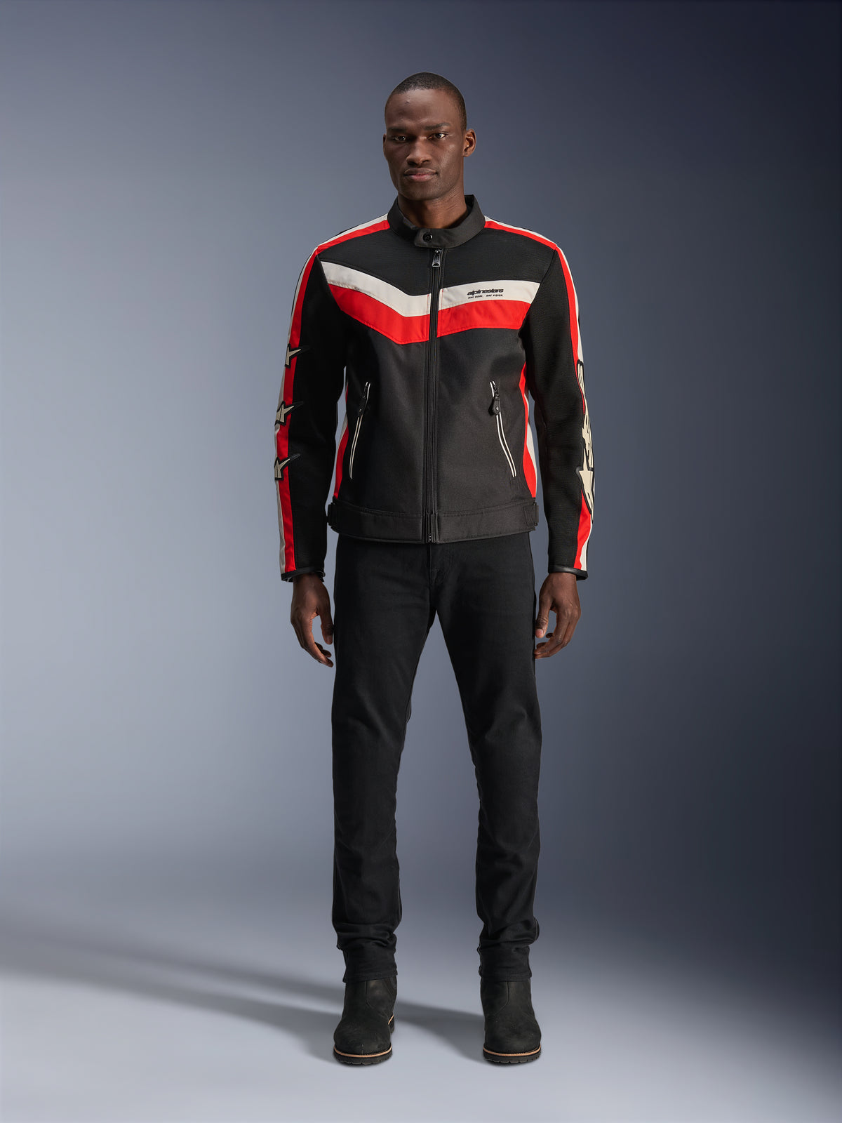 Chaqueta Alpinestars T-Dyno Air, chaqueta textil para moto, negro, rojo brillante y crudo, usada por un modelo con pantalones y botas negros, con un diseño de inspiración vintage con franjas de colores llamativos en el pecho, logos de estrellas en las mangas y construcción de malla transpirable para conducción urbana