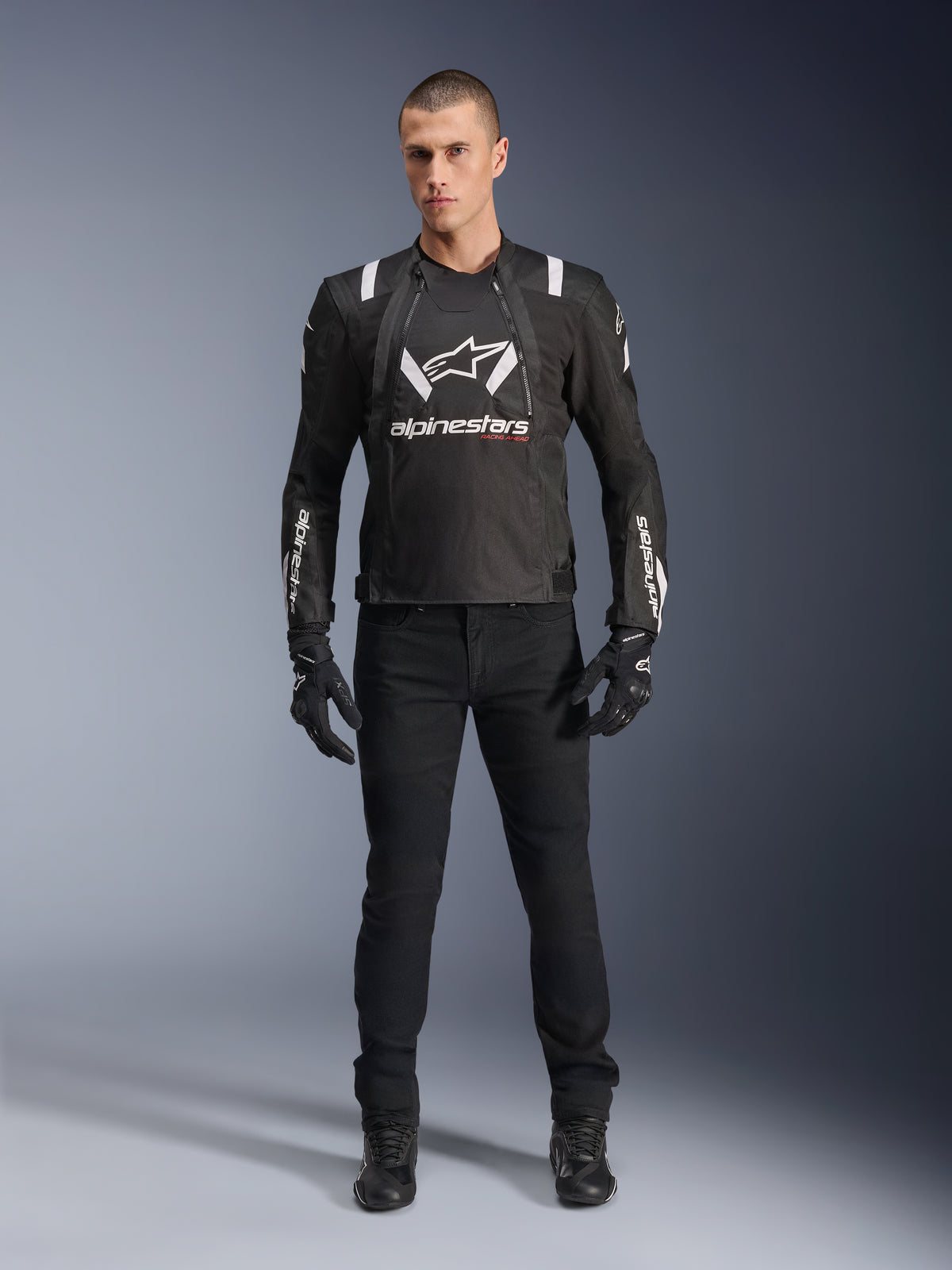 Alpinestars T-Stunt Air Jacket, Black and White motorcycle jacket, worn with black riding pants, gloves, and boots, featuring bold white Alpinestars branding on the chest and sleeves, sport-cut textile design with mesh panels for ventilation