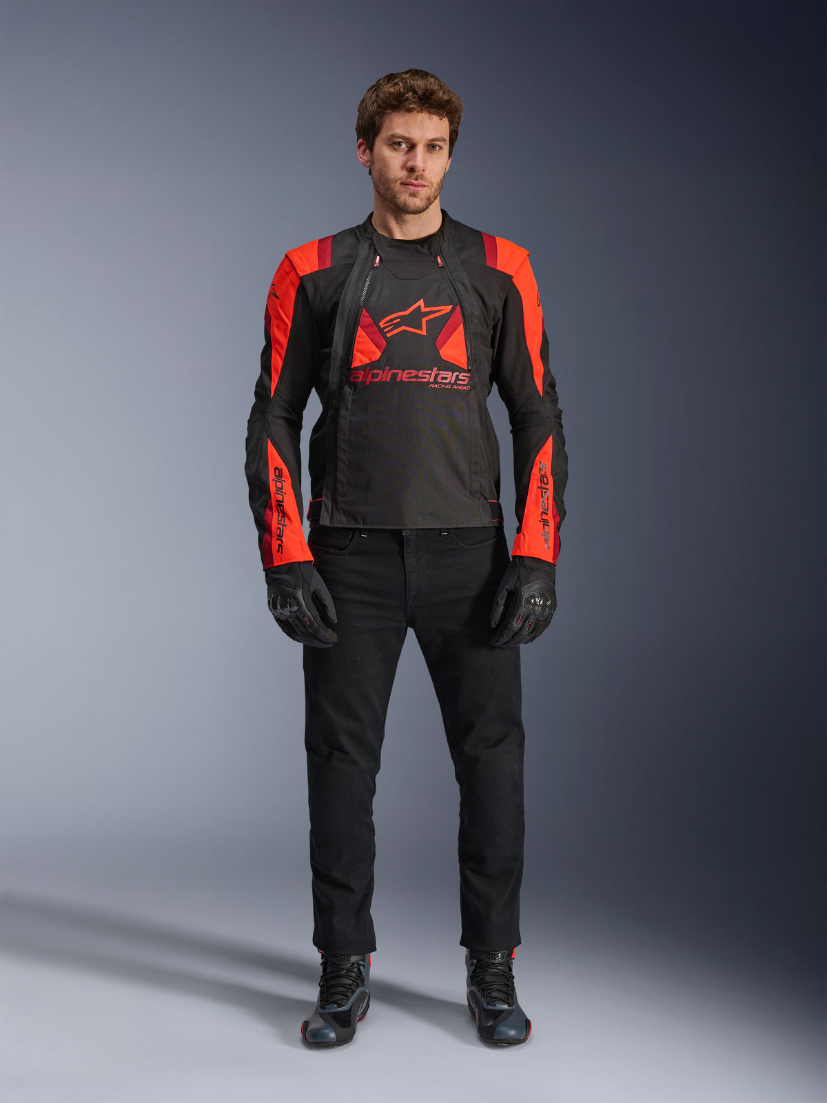 Chaqueta Alpinestars T-Stunt Air, negro, rojo fluo y rojo oscuro, usada por un modelo con vaqueros de moto negros y guantes, diseño modular 2 en 1 con paneles de malla prominentes para flujo de aire, equipamiento de moto de corte deportivo para carretera