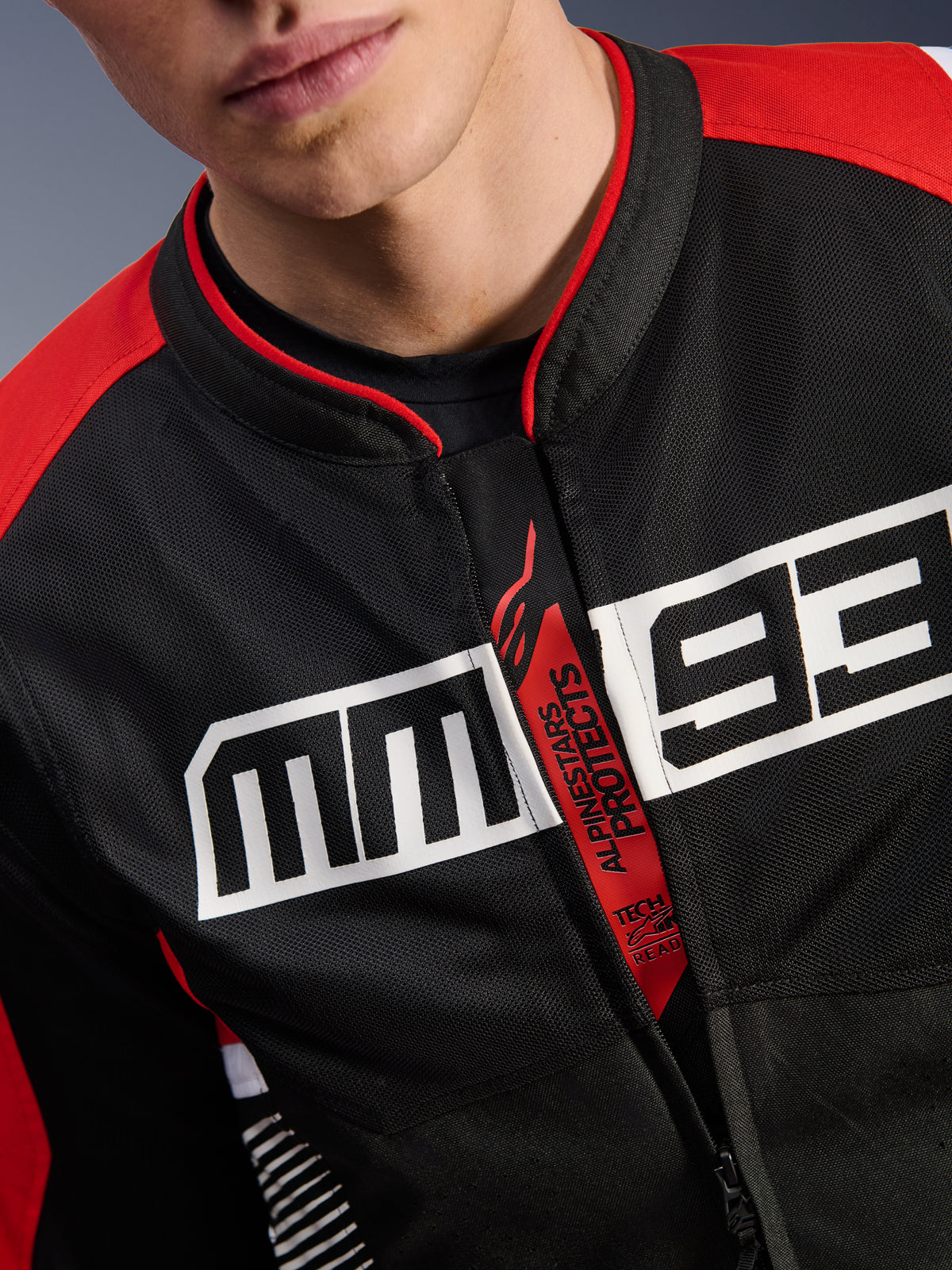 Alpinestars MM93 T-SPS Air V2 Jacket, Motorcycle Jacket, Black Bright Red and White, close-up of chest featuring large white MM93 logo, red 'Alpinestars Protects' and 'Tech-Air Ready' zipper pull, tech mesh fabric texture