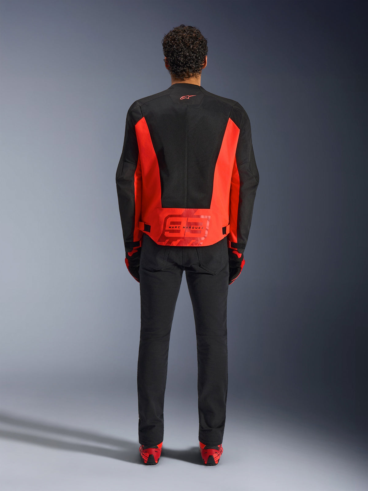 Alpinestars MM93 C-1 Air Jacket, chaqueta de motociclista, rojo flúor y negro, vista trasera con el gráfico de Marc Márquez 93 en la parte inferior de la espalda, paneles de malla técnica para ventilación, combinada con pantalones negros y equipamiento con detalles rojos