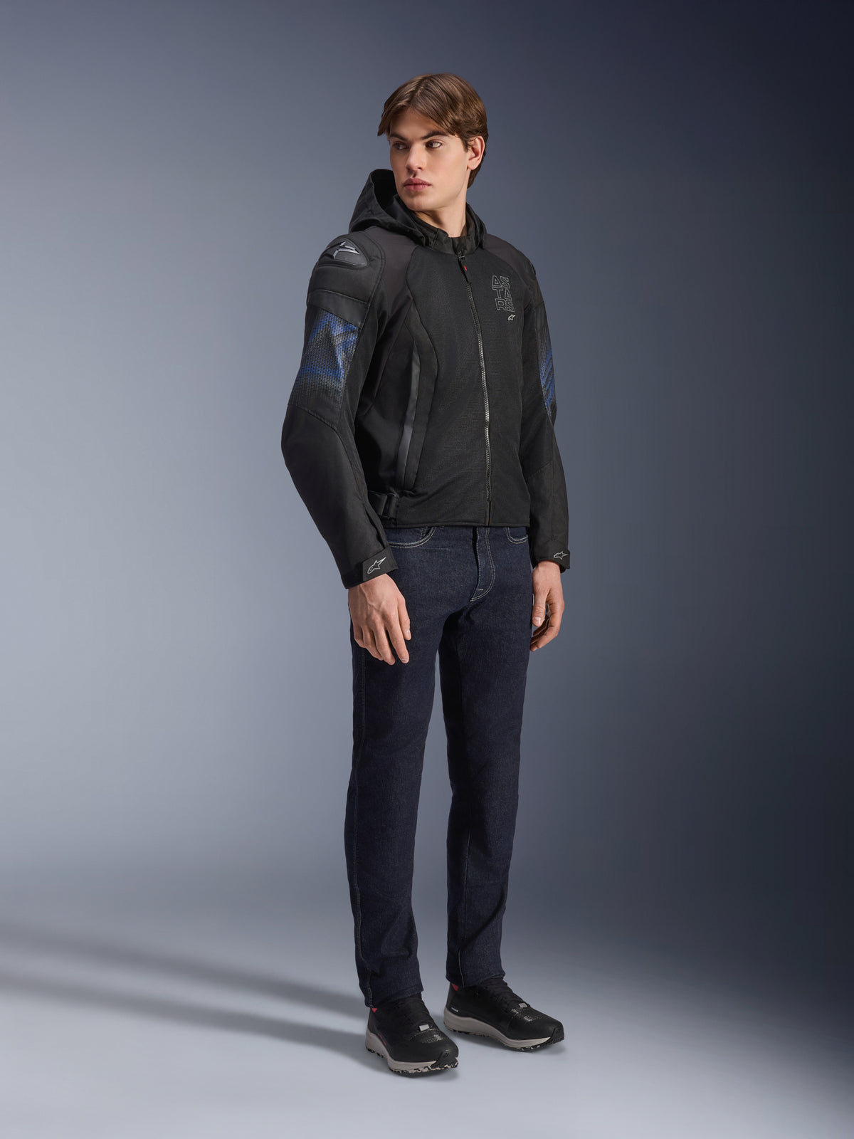 Chaqueta Alpinestars Zaca Air Venom WP, chaqueta de moto textil en color negro y azul eléctrico, usada por un modelo con vaqueros oscuros y zapatillas negras, con capucha desmontable, paneles de ventilación de malla y deslizadores de hombro DFS Lite, equipamiento deportivo para todo tipo de clima