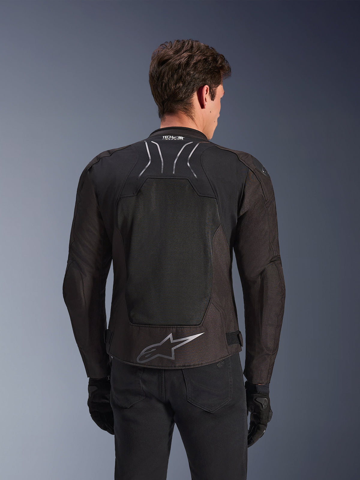 Alpinestars SMX Air Jacket in Black Anthracite, rear view on a model, featuring a large tech mesh back panel for ventilation, Tech-Air Ready branding on the collar, and a silver Astar logo on the lower back, paired with black gloves and riding trousers.