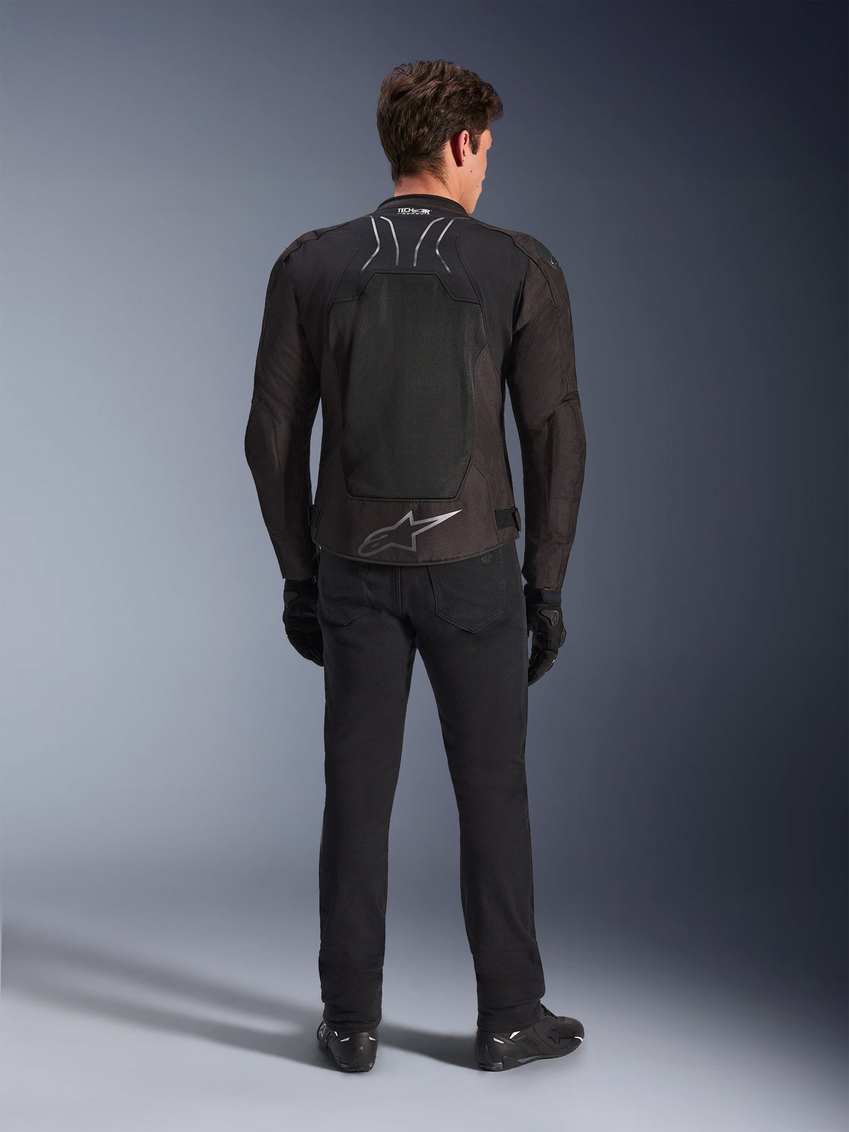 Alpinestars SMX Air Jacket, Black Anthracite, back view on male model, featuring a large silver Alpinestars logo on the lower back and high-flow mesh paneling, worn with black riding pants, gloves, and boots, sport motorcycle gear