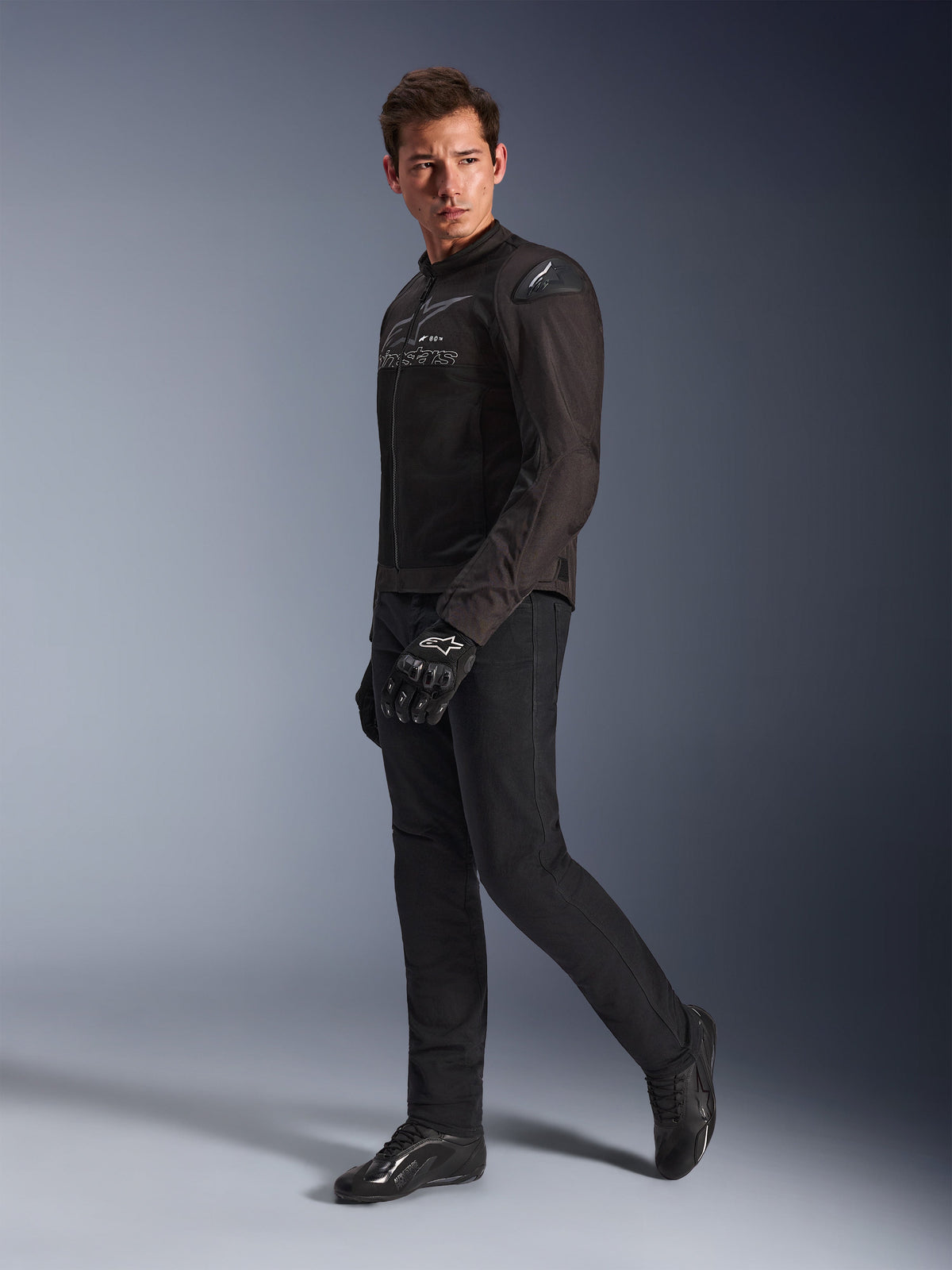 Alpinestars SMX Air Jacket in Black Anthracite, worn by model with matching black riding pants, gloves, and shoes, studio full-body shot, performance sport motorcycle gear featuring tech mesh and shoulder sliders