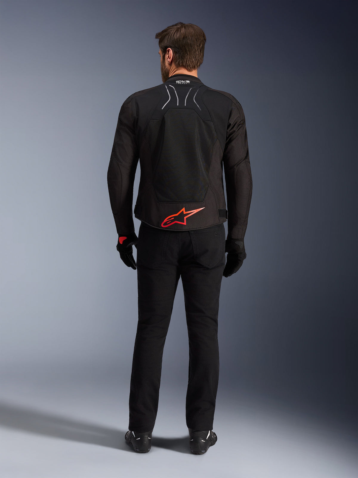 Chaqueta Alpinestars SMX Air, negra con logo en rojo brillante, vista trasera que muestra la marca Tech-Air Ready y paneles de ventilación de malla, combinada con pantalones y guantes negros, equipamiento de alto rendimiento para motociclismo deportivo y de carreras