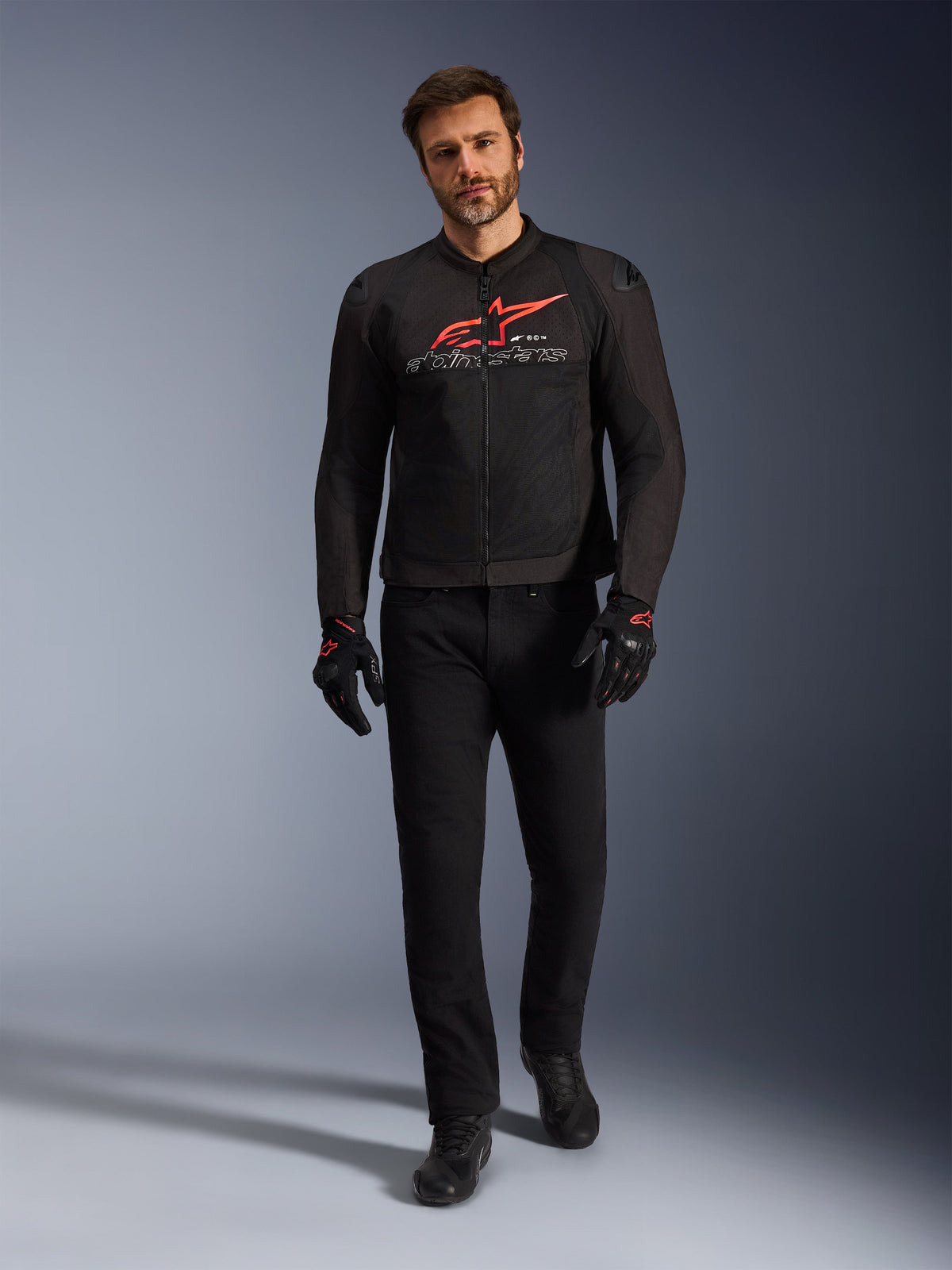 Chaqueta Alpinestars SMX Air, negro, rojo brillante y blanco, chaqueta de moto deportiva usada con pantalones y guantes negros, con paneles de malla técnica y un llamativo logotipo rojo de Alpinestars en el pecho, conjunto de conducción urbana de alto rendimiento