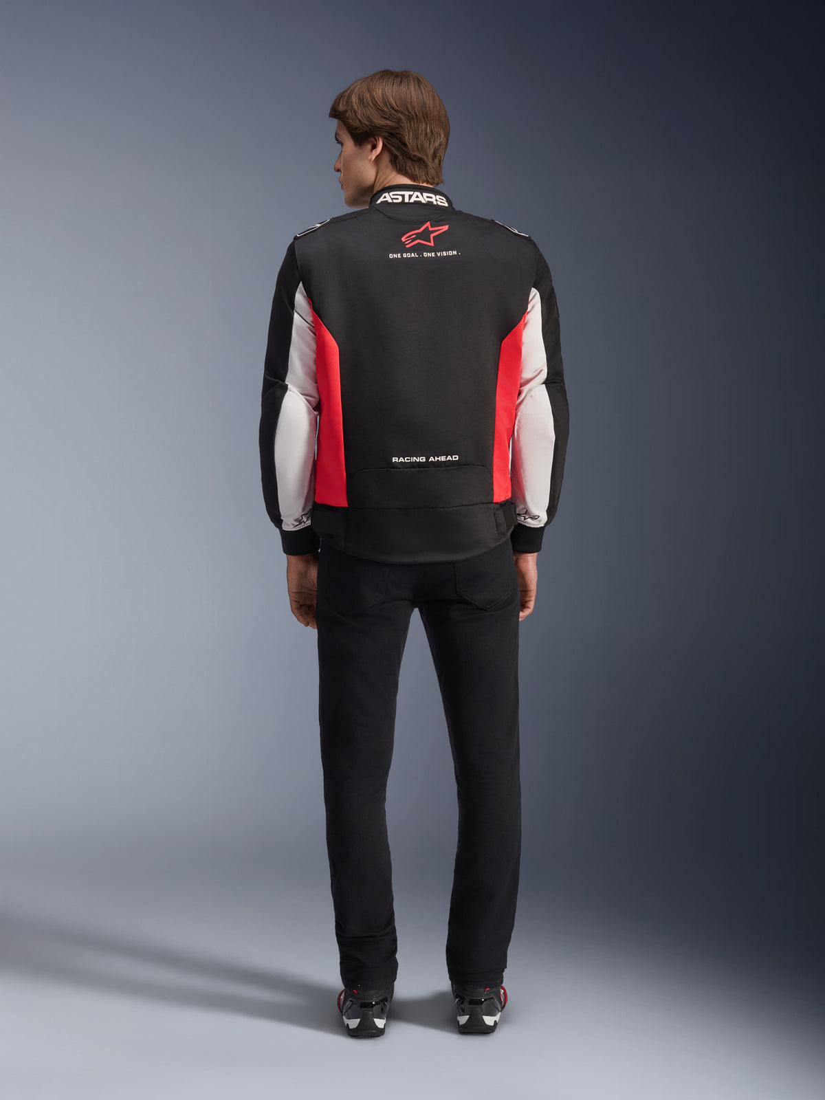 Alpinestars Monza Sport Jacket, Black Bright Red and White textile motorcycle jacket, rear view shown on a model, featuring red star logo and 'ASTARS' collar branding with slogans, worn with black pants and riding boots.