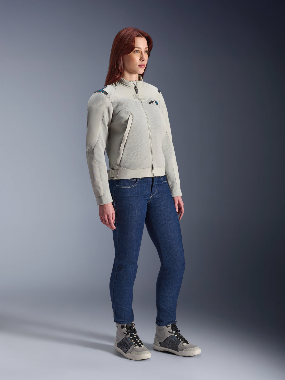 Mujer vistiendo la chaqueta Alpinestars Stella Circal-1 Air en Metal Gray y Methyl Blue, combinada con vaqueros azules y calzado casual para moto, mostrando los paneles de malla y el diseño urbano minimalista de la chaqueta.
