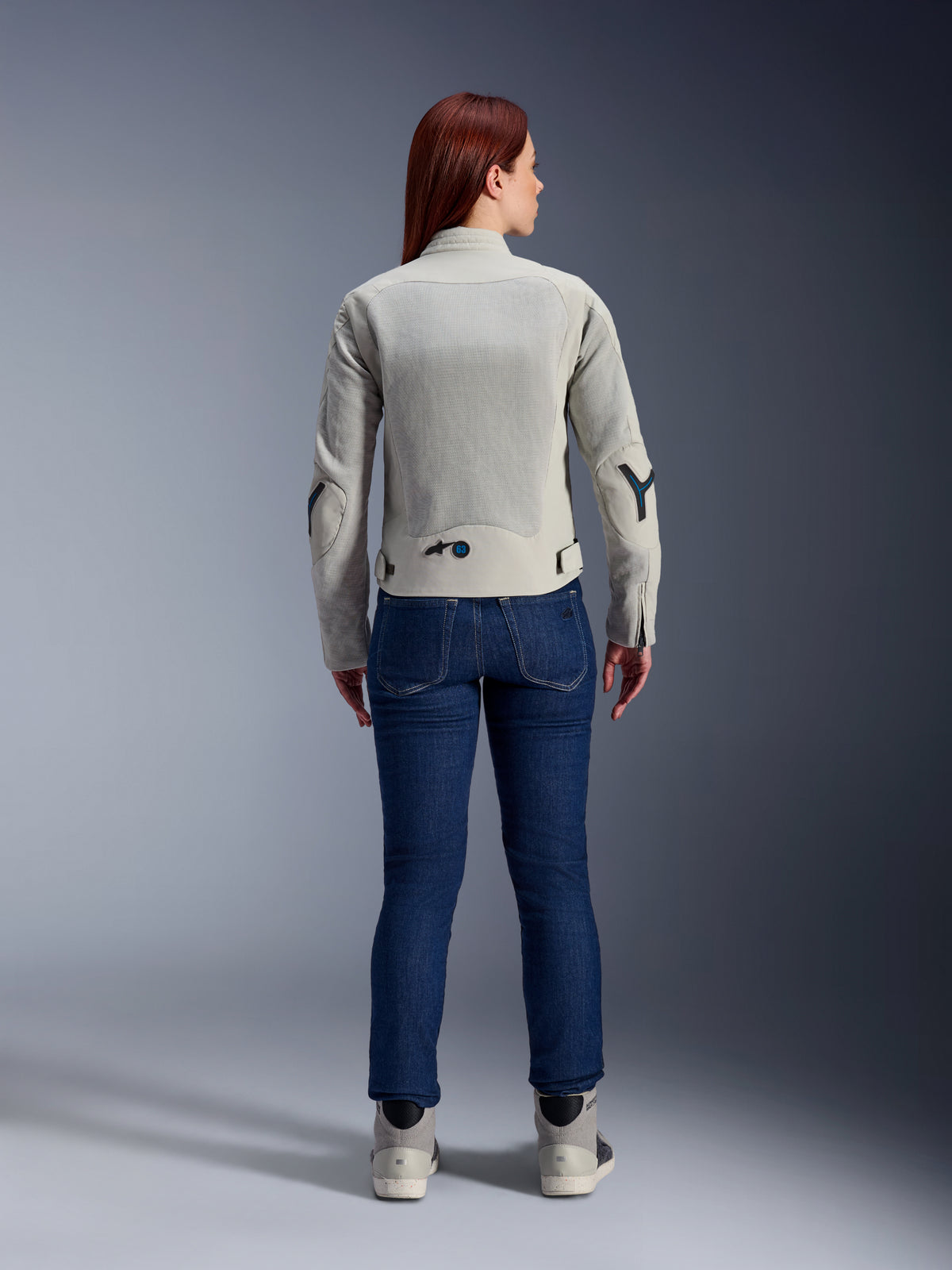 Chaqueta para mujer Alpinestars Stella Circal-1 Air en gris metalizado y azul methyl, vista trasera, con amplios paneles de malla para el flujo de aire en la espalda y los brazos, combinada con vaqueros de denim azul oscuro y calzado de moto gris para un look urbano moderno.