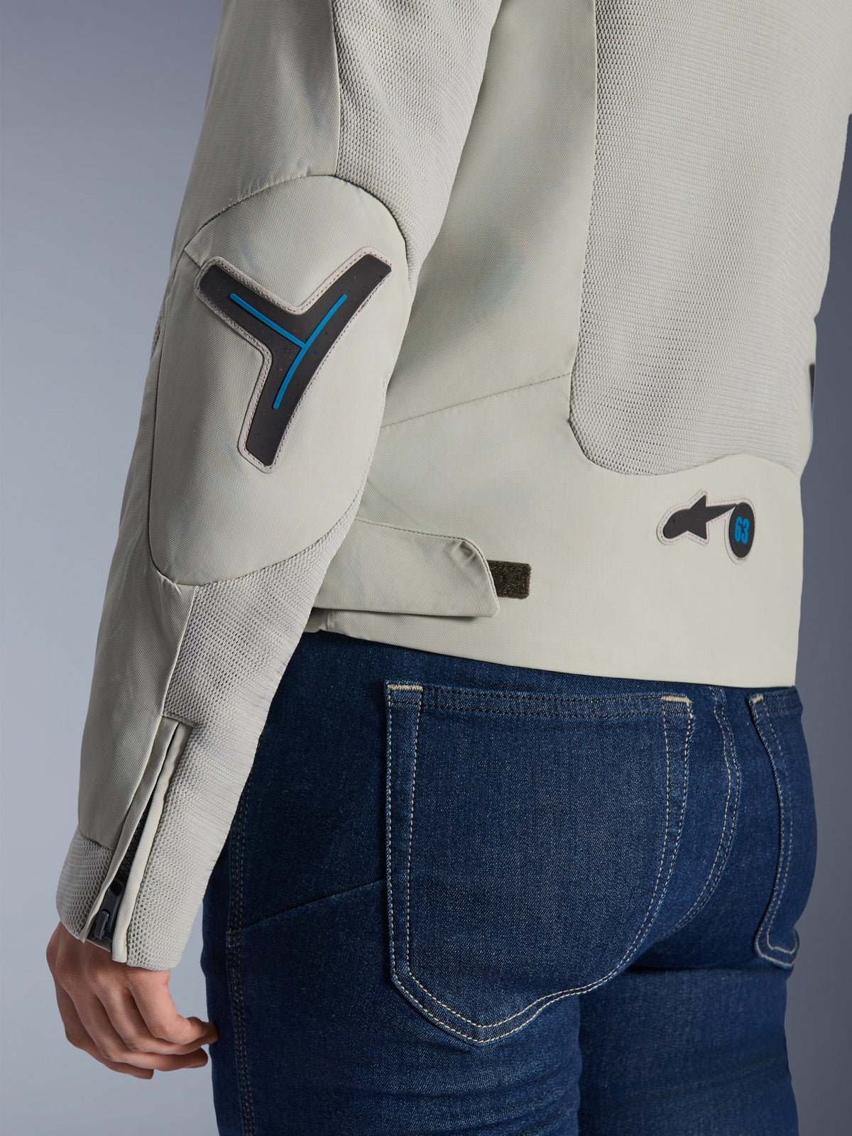 Chaqueta Stella Circal-1 Air de Alpinestars para mujer en gris metalizado y azul metilo, primer plano del detalle de la espalda y la manga que muestra los paneles de malla de flujo de aire, detalles en azul neón en el codo y la cintura, y lengüeta ajustable, usada con pantalones vaqueros azul oscuro.