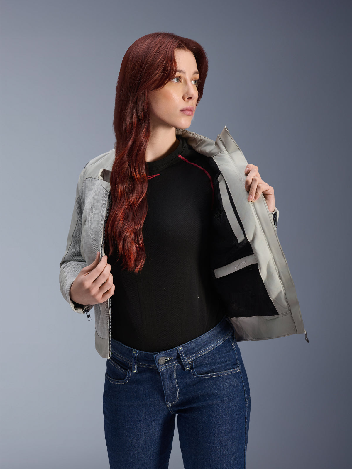 Chaqueta Alpinestars Stella Circal-1 Air en Metal Gray, modelo femenina abriendo la chaqueta para mostrar el forro de malla interno y el bolsillo, combinada con vaqueros azules y un top negro, equipamiento de motociclismo urbano contemporáneo.