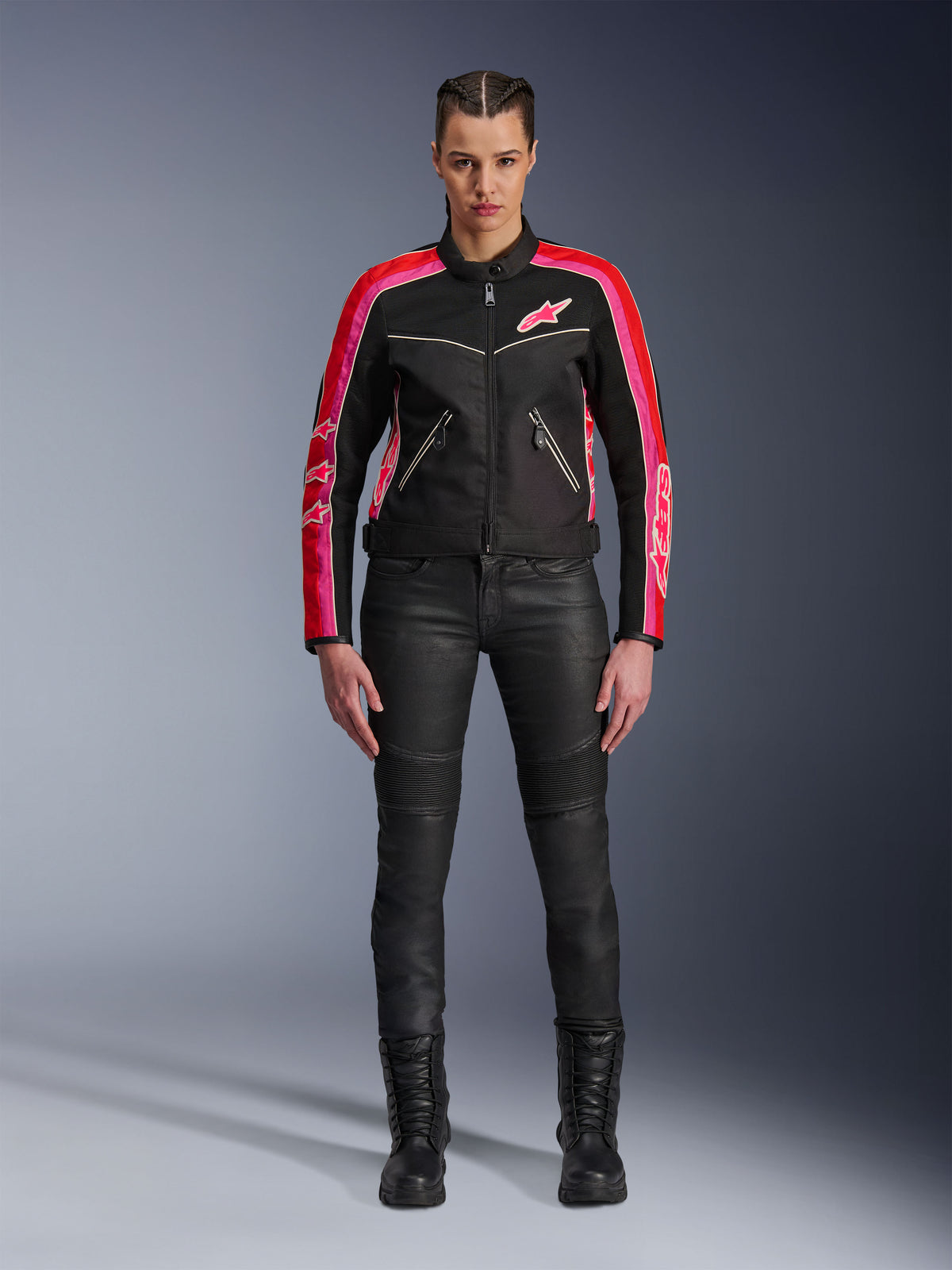 Mujer motociclista con la chaqueta Alpinestars Stella T-Dyno Air, negra con detalles en rojo brillante y fucsia, combinada con pantalones de moto negros y botas con cordones, con paneles de malla 3D, ajuste entallado y logotipos de estrellas rosas, conjunto de equipamiento para conducción urbana