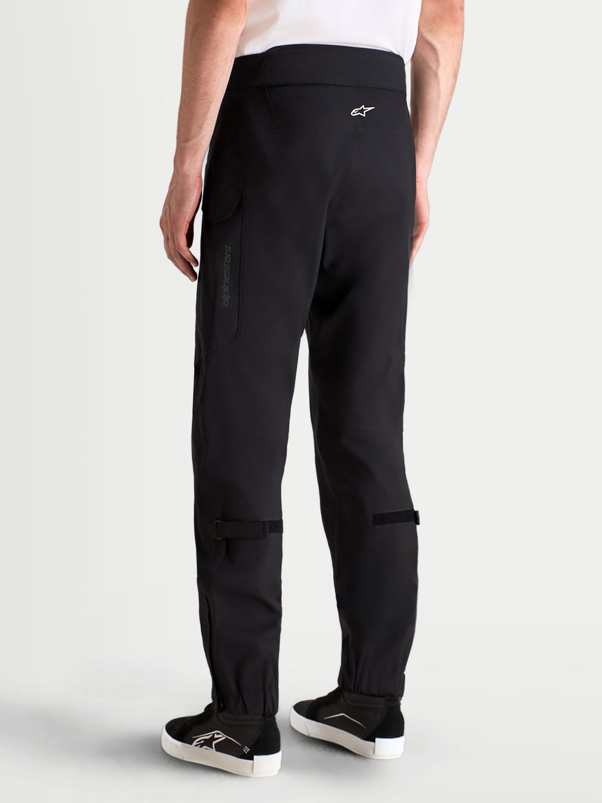 Alpinestars Juggernaut V2 Drystar® Pants, men's waterproof urban motorcycle riding pants in black, rear profile view on a model wearing matching gear and boots, featuring high-back waistband and cargo pockets.