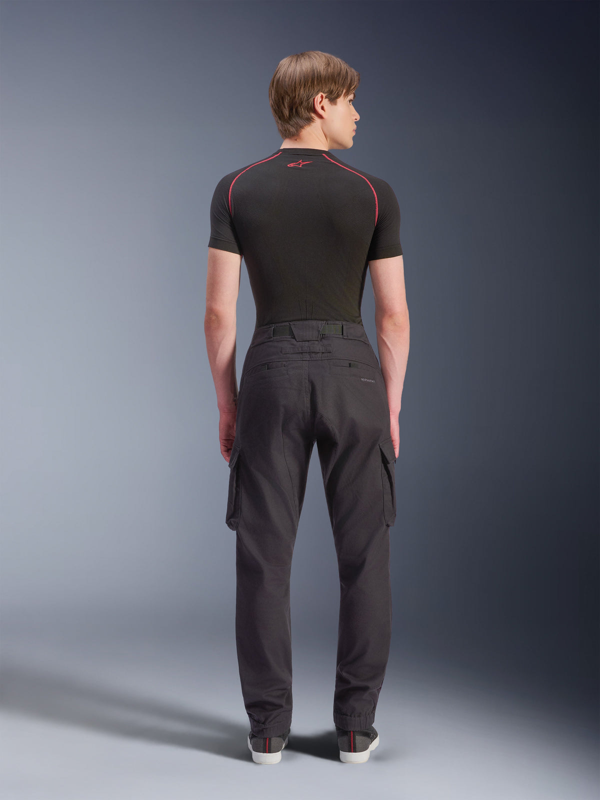 Alpinestars Flex-AST Cargo Pants - Short, negros, pantalones urbanos de motociclismo vistos desde atrás, con bolsillos cargo laterales y dobladillos elásticos, combinados con una prenda base negra de manga corta con costuras rojas en contraste