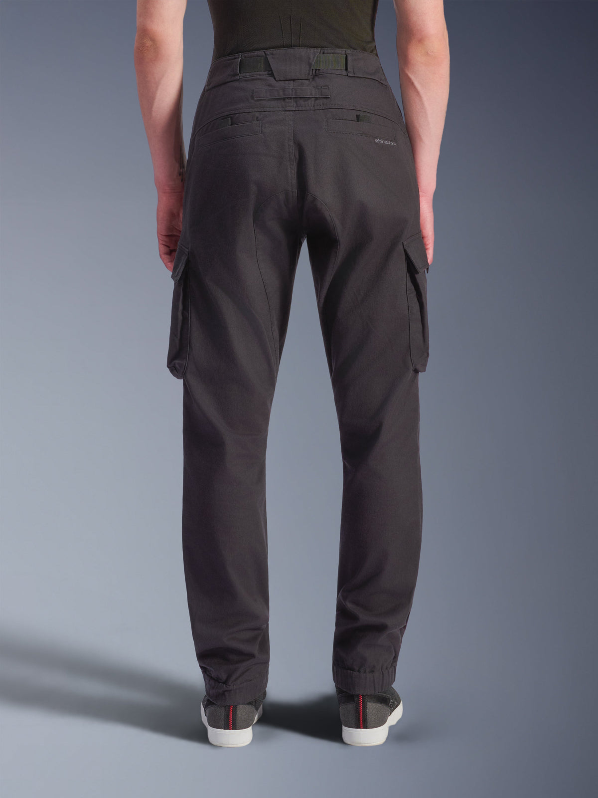 Pantalones Cargo Alpinestars Flex-AST - Cortos, pantalones de moto urbanos, negros, vista trasera que muestra un ajuste regular tapered con dobladillos elásticos, grandes bolsillos cargo laterales y marca sutil en el bolsillo trasero, usados con zapatillas casuales