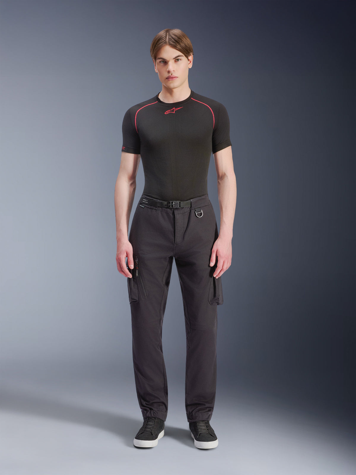 Pantalones Cargo Alpinestars Flex-AST - Cortos, negros, lucidos por un modelo masculino con una camiseta técnica negra y zapatillas negras; pantalones de moto urbanos con múltiples bolsillos cargo, ajuste cónico y cinturón integrado con hebilla y anilla en D