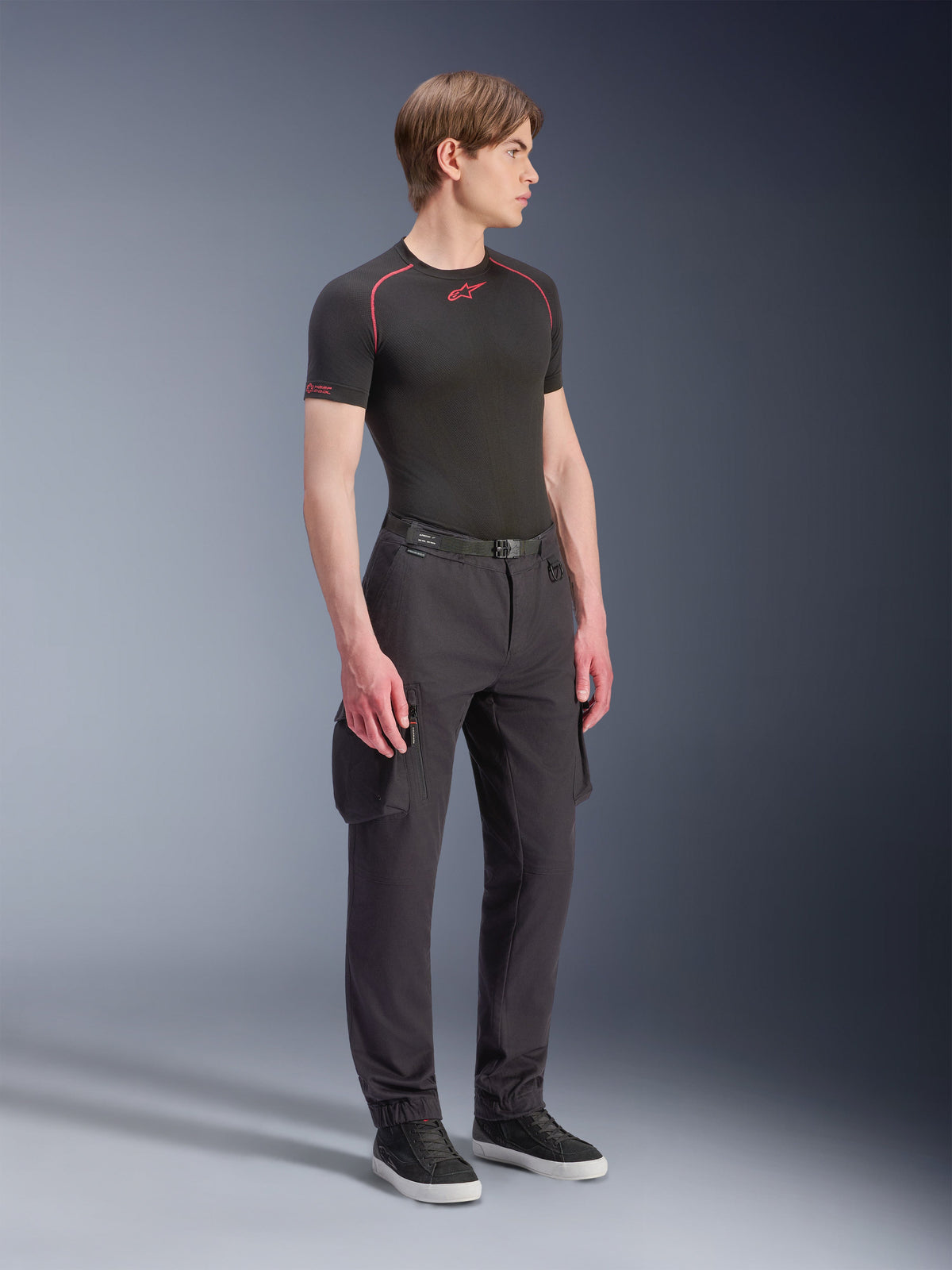 Modelo masculino vistiendo los pantalones cargo Alpinestars Flex-AST - Cortos en color negro, pantalones cargo urbanos para moto con bolsillos laterales y piernas de corte cónico, combinados con una capa base negra y zapatillas, indumentaria de conducción urbana.