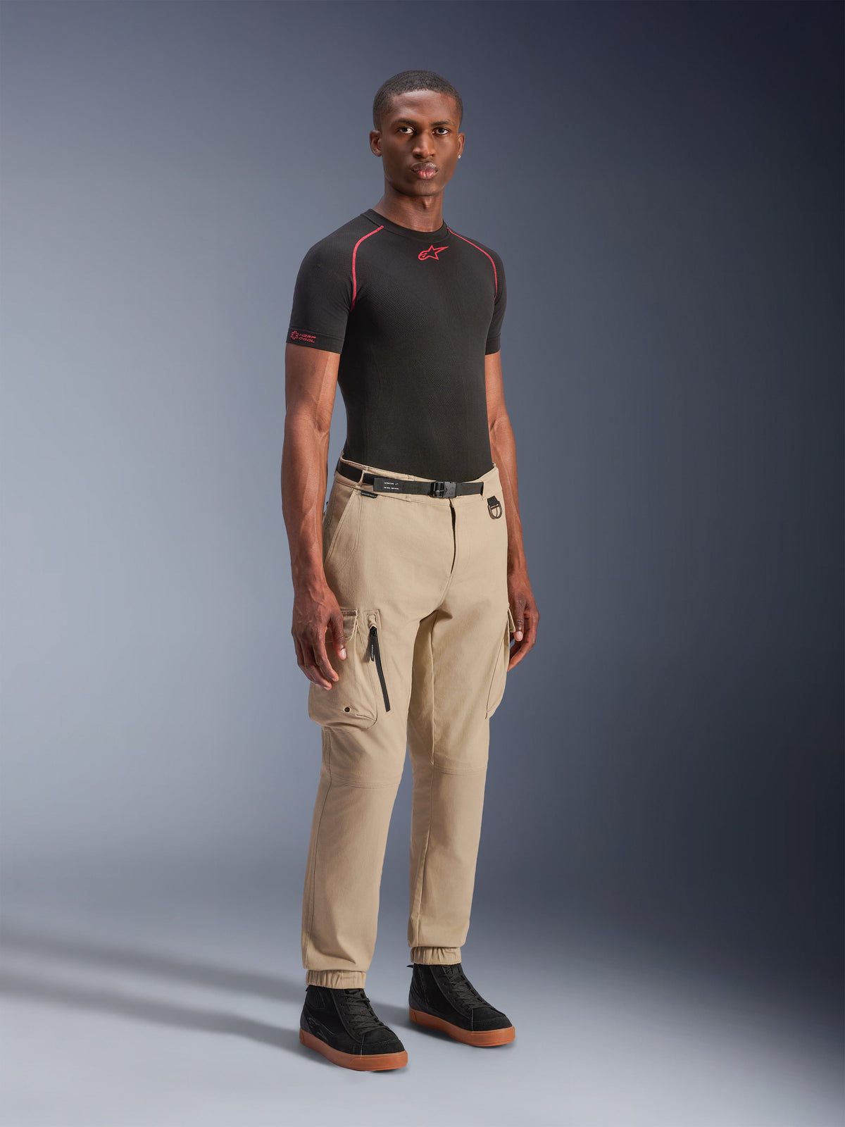 Alpinestars Flex-AST Cargo Pants - Short, pantalones de moto urbanos en beige claro, usados por un modelo con una capa base negra y zapatillas, con un ajuste cónico regular, dobladillos elásticos y diseño cargo con múltiples bolsillos