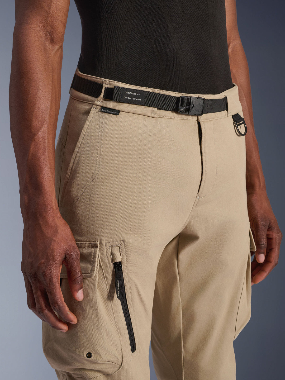 Pantalones Cargo Alpinestars Flex-AST - Cortos, beige claro, vista detallada de la cintura y el muslo, con cinturón ajustable negro con la marca Alpinestars, anillo en D metálico y bolsillos cargo funcionales con cremalleras y solapas con botones de presión, equipamiento para moto urbano contemporáneo