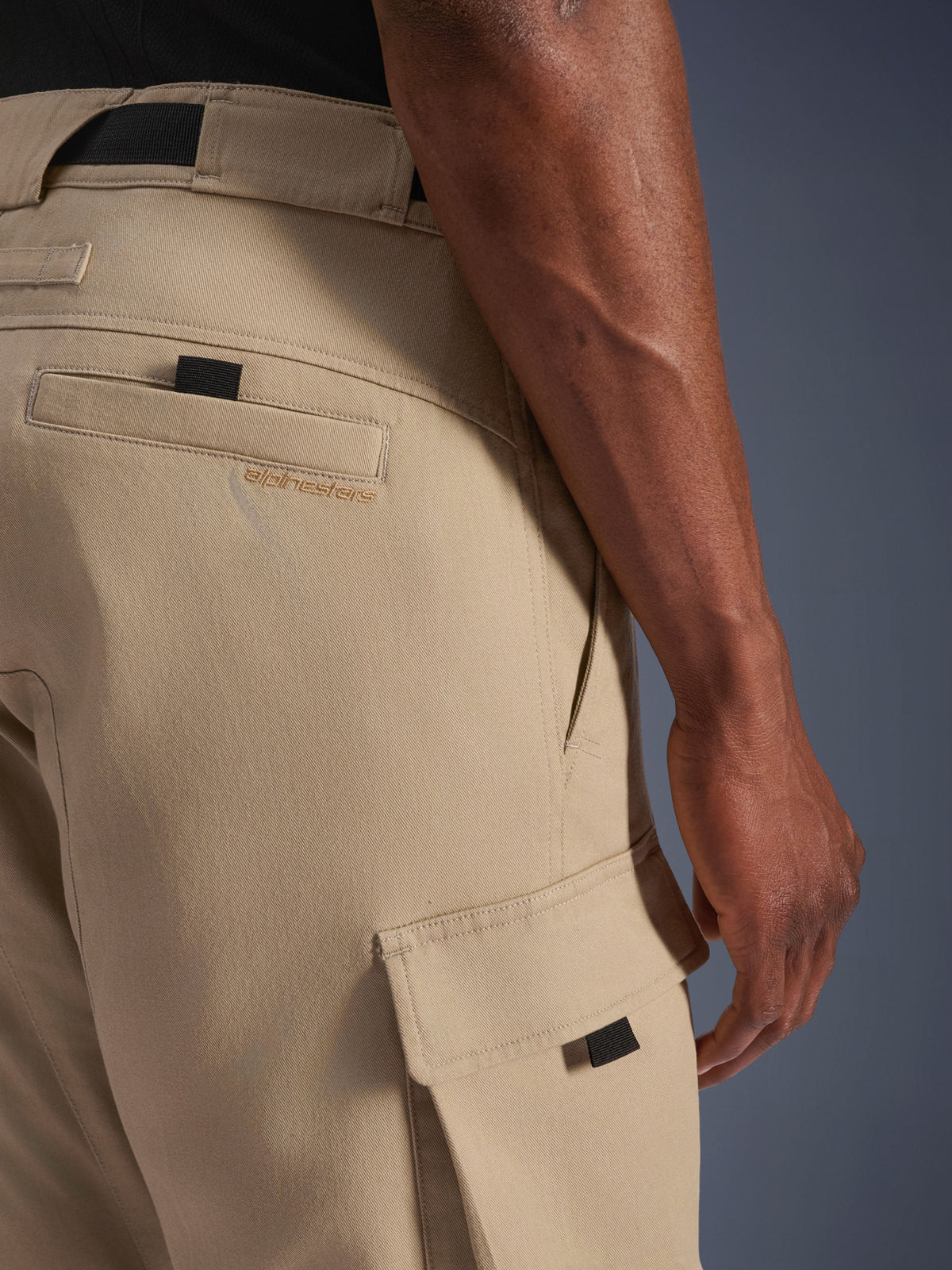 Alpinestars Flex-AST Cargo Pants - Cortos, beige claro, primer plano lateral que muestra el bolsillo cargo con tirador negro y el logotipo bordado en el bolsillo trasero, material textil duradero, equipamiento urbano para motociclista.