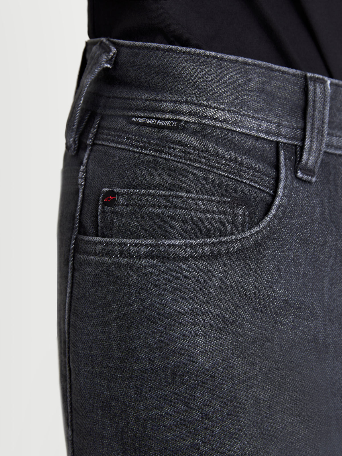 Alpinestars Flex Ast 7 Denim Pantalones, pantalones vaqueros de moto urbanos para hombre en negro descolorido, vista en primer plano que muestra la construcción del bolsillo, detalle de remache con marca y etiqueta tejida Alpinestars Protects