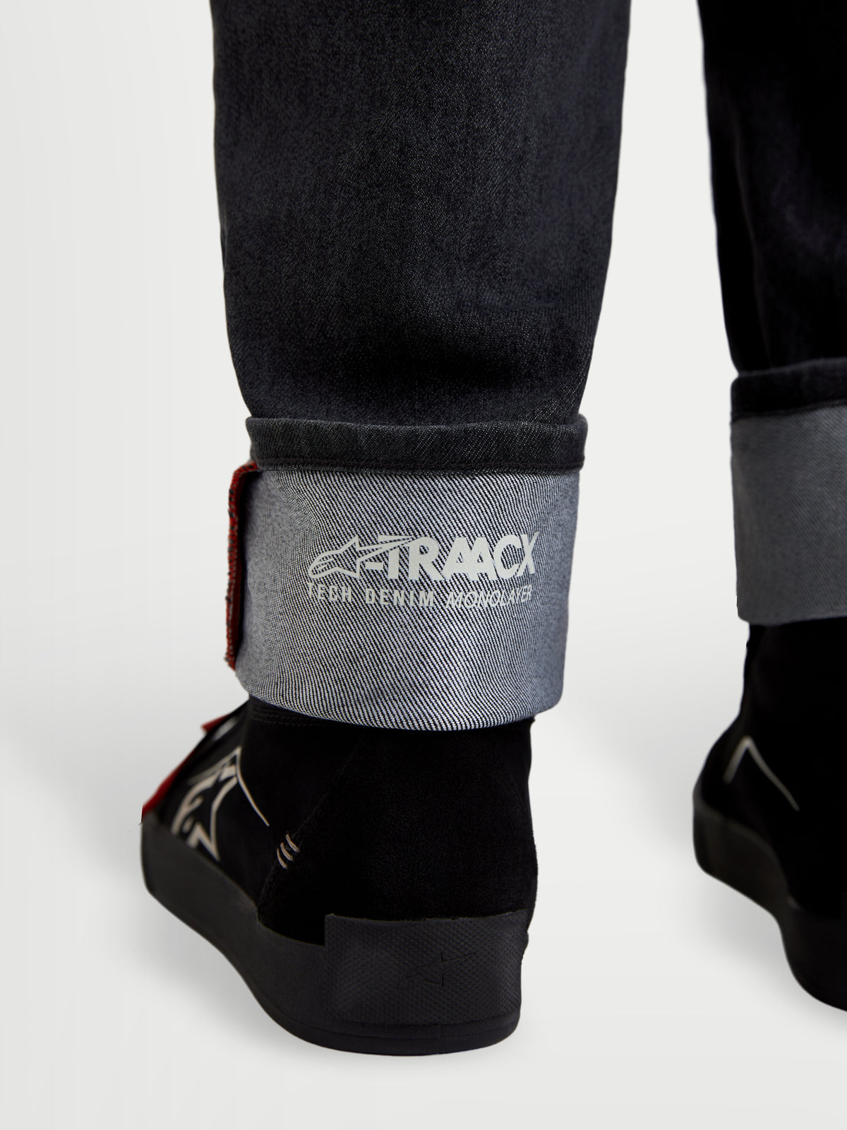 Alpinestars Flex Ast 7 Denim Pantalones, pantalones de moto de denim en negro desgastado, vista en primer plano del dobladillo con vuelta que muestra la marca A-TRAACX technical denim y el detalle de selvedge