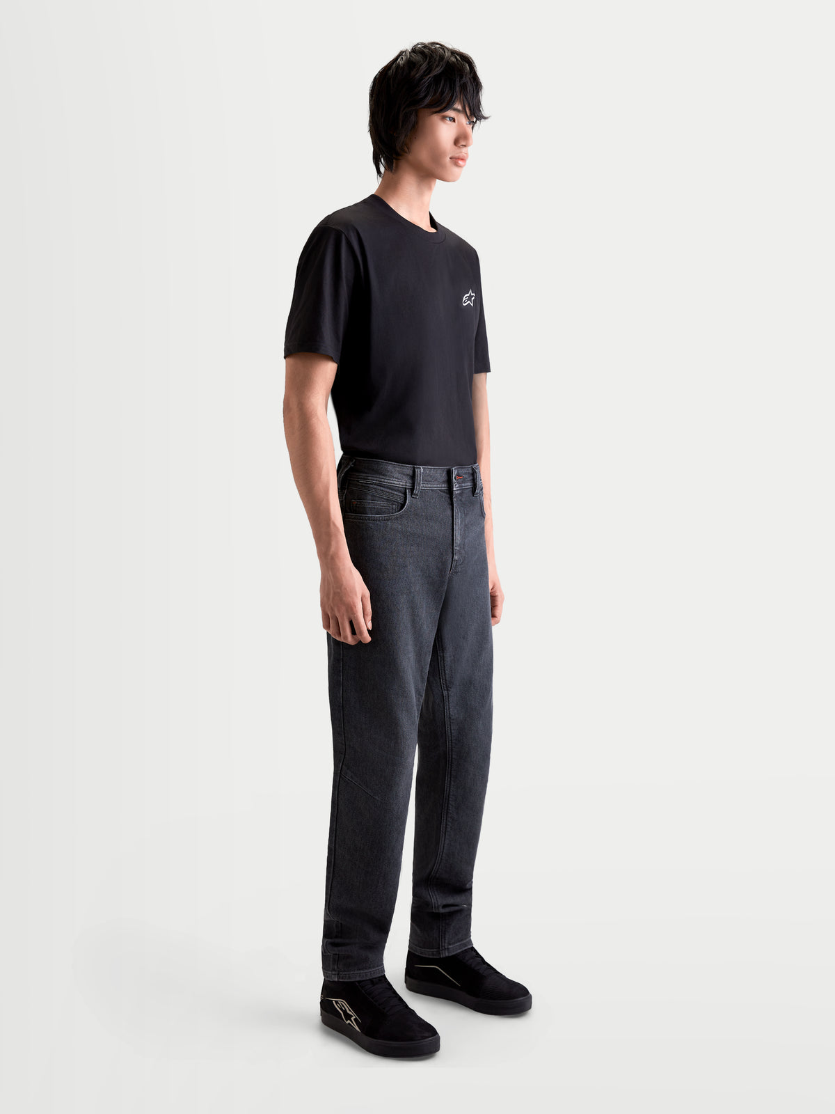 Alpinestars Flex Ast 7 Denim Pantalones, pantalones de moto urbanos para hombre en negro desgastado, vista lateral en modelo con camiseta negra, construcción de denim técnico monocapa certificado AA