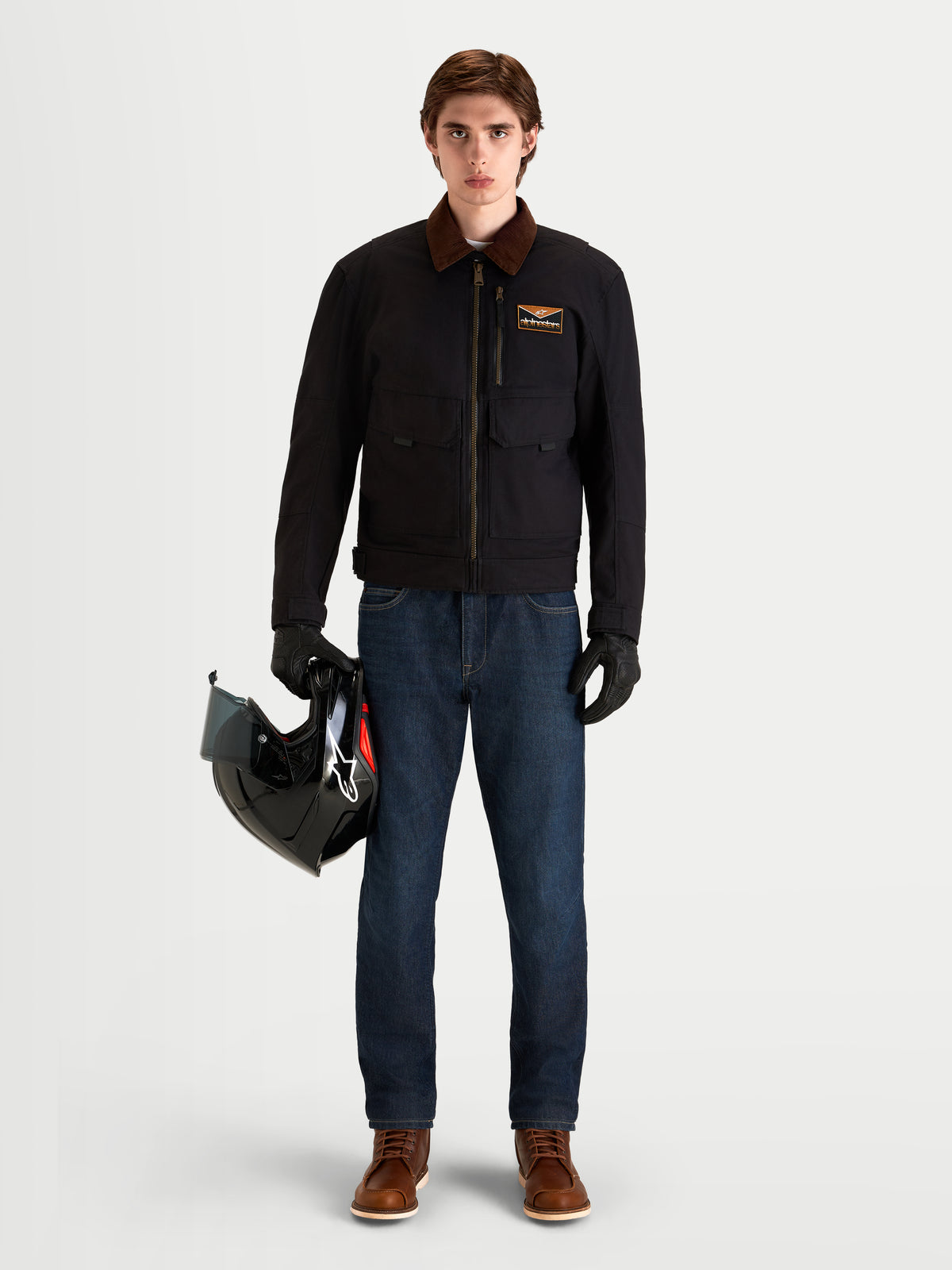 Alpinestars Flex-AST 7 Denim Pants, men's urban motorcycle riding jeans in dark blue, shown on a model wearing a black jacket with brown collar and holding a helmet
