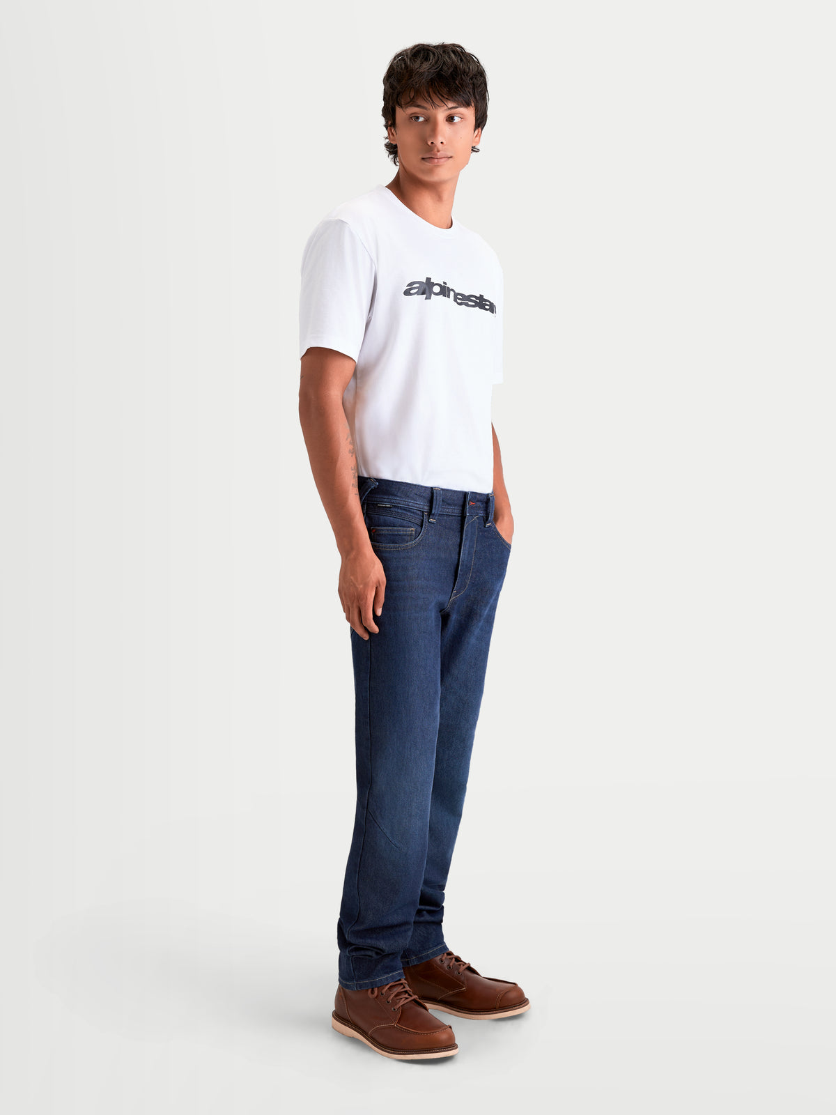 Alpinestars Flex-AST 7 Denim Pants, men's urban contemporary motorcycle riding jeans in dark blue, side profile view worn by a model wearing a white t-shirt and brown boots, featuring AA-rated single-layer CORDURA® construction.
