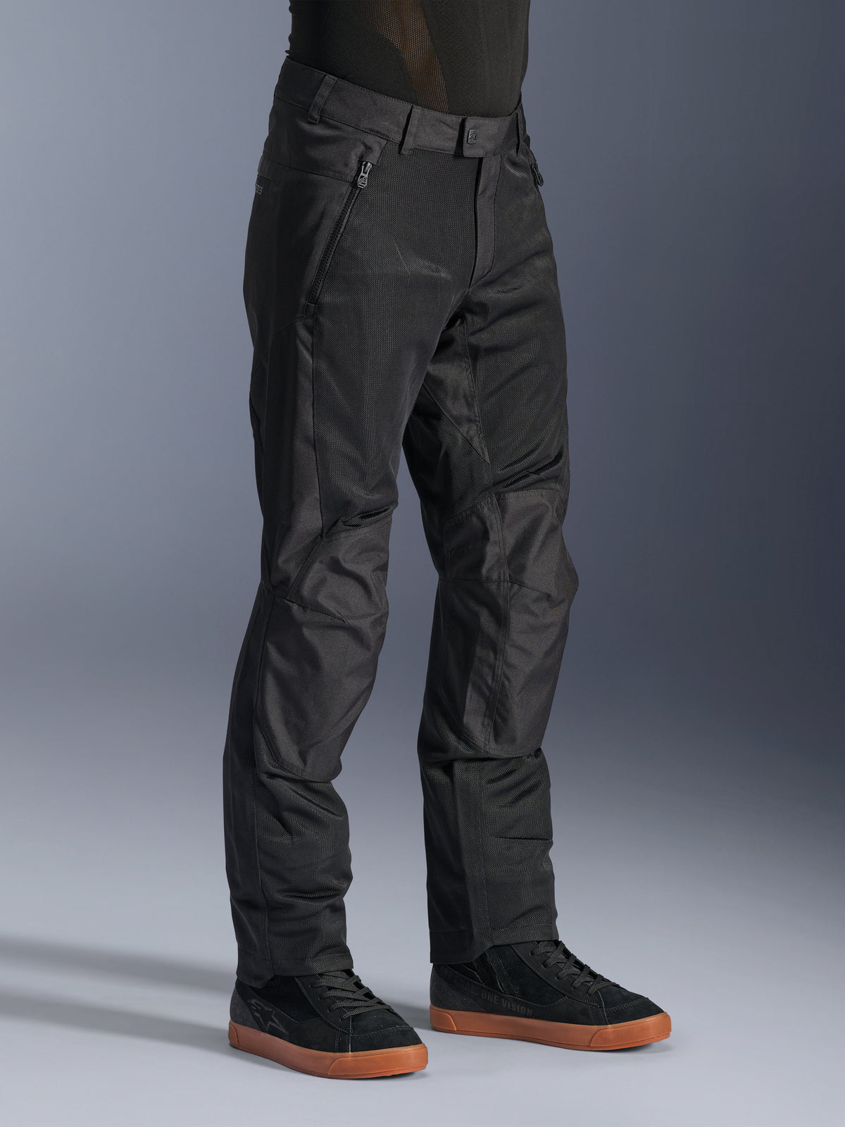 Alpinestars C-1 Air Pants, pantalones urbanos de moto, negros, con paneles de malla técnica transpirable y construcción en polifabric, usados con zapatillas negras, diseño limpio y funcional para la conducción urbana.