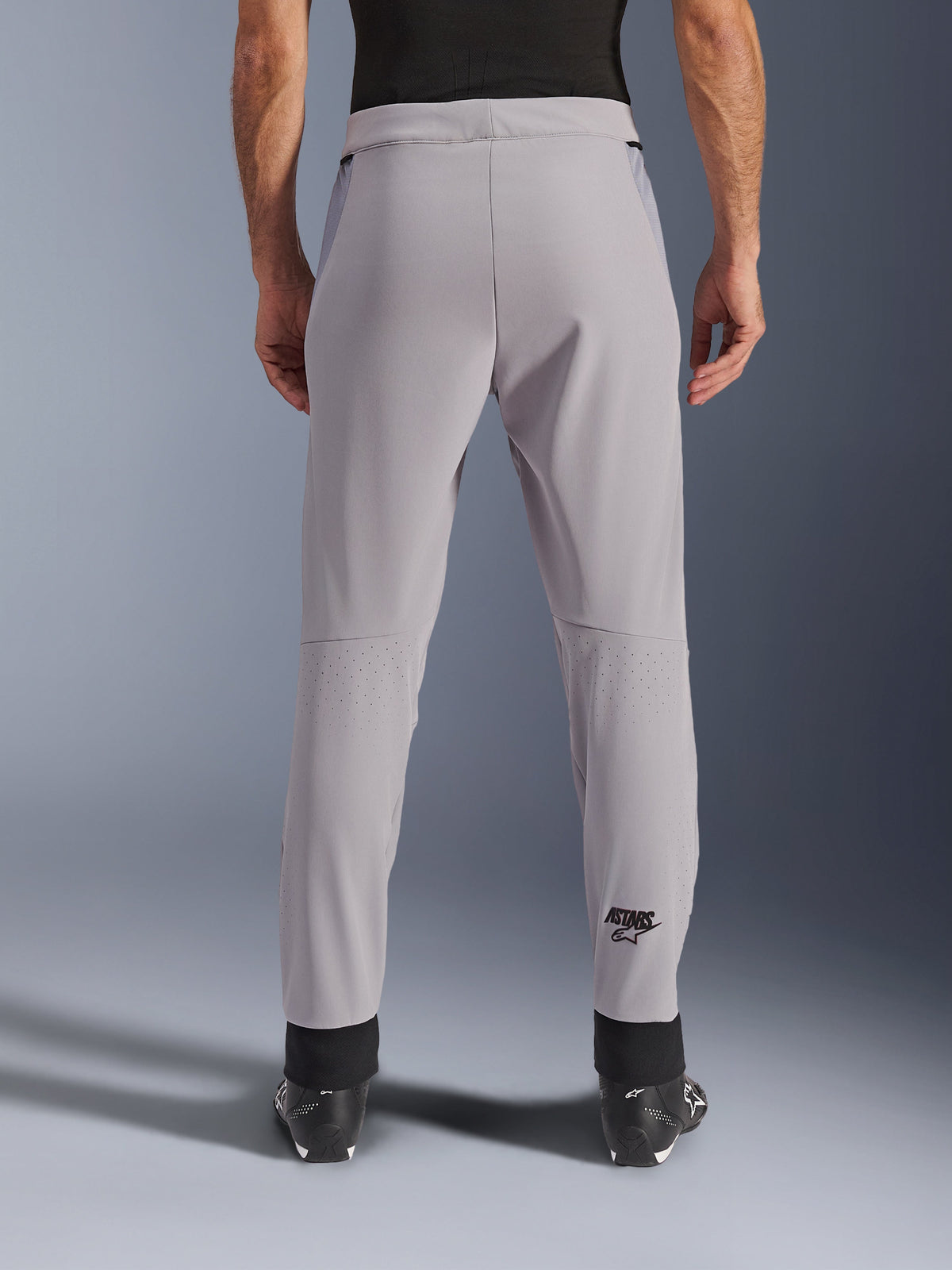 Pantalones Alpinestars Aeroshell Airflow, pantalones de moto, Mid Gray, vista trasera que muestra las zonas perforadas con láser en las pantorrillas y el logotipo negro de Astars, confección en softshell textil con puños negros en los tobillos y paneles de malla en la cadera.