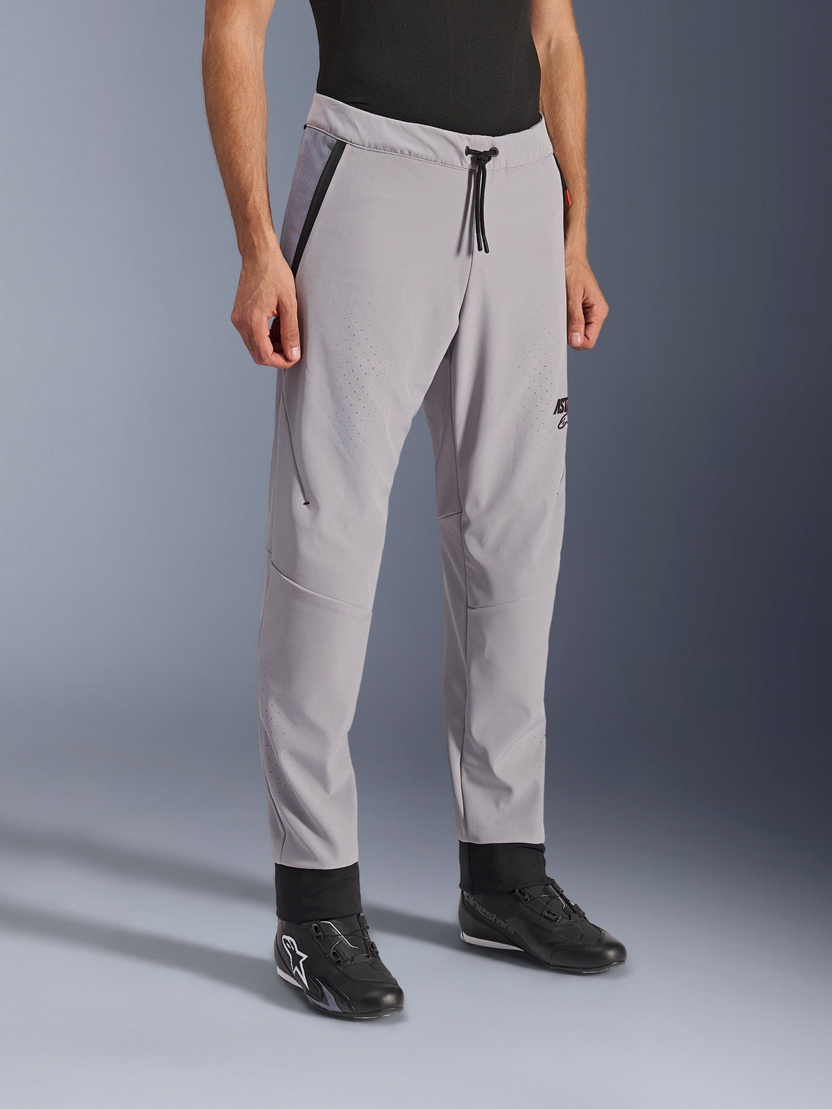 Pantalones Alpinestars Aeroshell Airflow, Gris Medio, pantalones de moto ligeros con zonas de ventilación perforadas con láser en los muslos y las espinillas, cuentan con una cintura elástica con cordón y un ajuste deportivo entallado, mostrados en un modelo con calzado de moto negro.