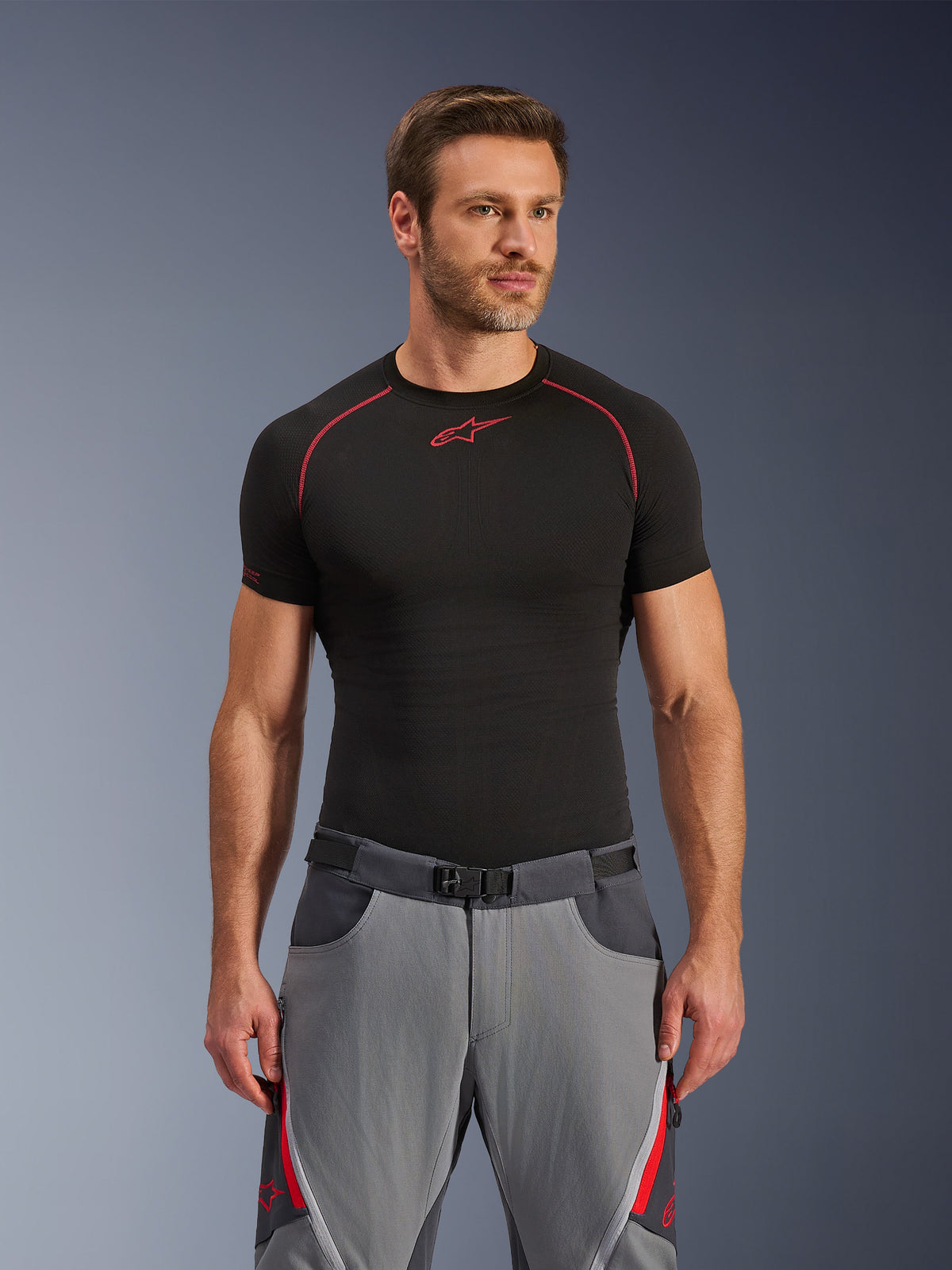 Alpinestars Maxdura Dual Pants, Dark Gray and Deep Gray with red accents, worn with a black base layer shirt featuring red stitching, athletic fit with integrated magnetic buckle belt, durable adventure motorcycle gear