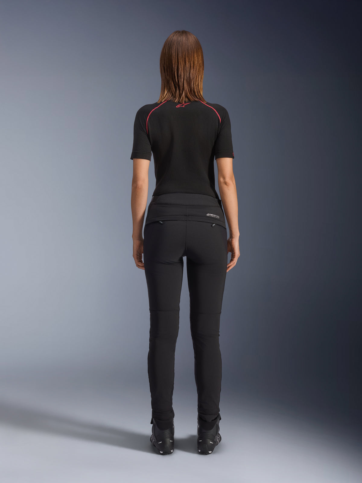 Alpinestars Alamosa Women Pants, Black, rear view showcasing slim-fit textile construction, zippered back pockets, and reflective MO.ST.EQ. branding on the back yoke, worn with a black short-sleeve base layer and black motorcycle boots