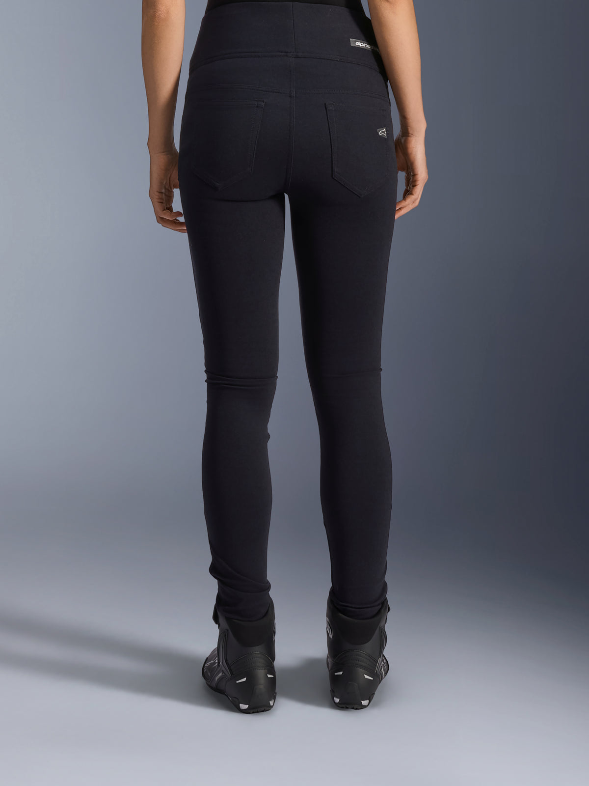 Leggings Alpinestars Stella Flex-Ast, leggings de moto para mujer, negros, vista trasera que muestra los bolsillos posteriores y el ajuste entallado, combinados con botas de moto negras, estilo de conducción urbana