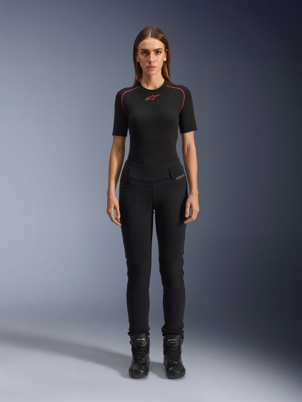 Leggings Banshee para mujer de Alpinestars, leggings de moto negros, ajuste anatómico ceñido, usados por una modelo con una capa base negra y botas de moto, con paneles acanalados en las rodillas y diseño de talle alto para conducción urbana.