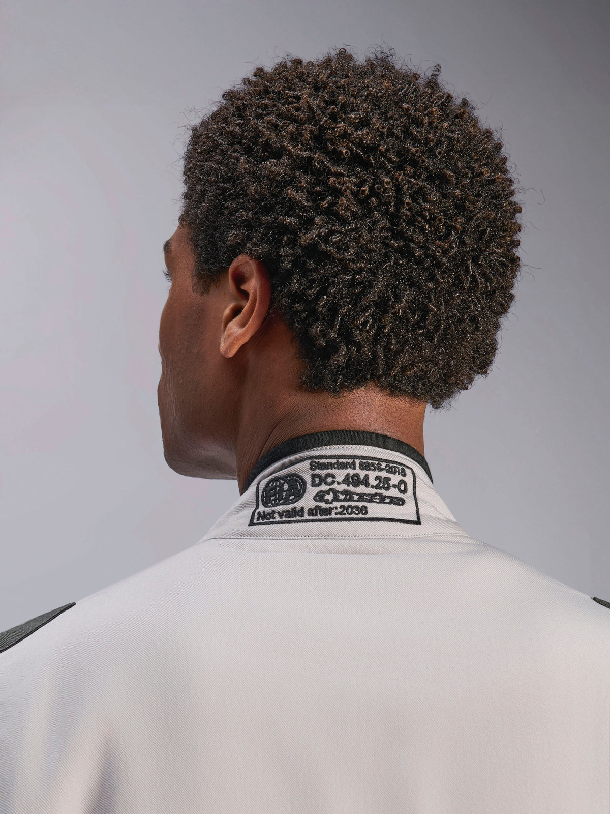 Alpinestars GP Race V3 Suit FIA, Silver Anthracite, primer plano del cuello posterior con la etiqueta de certificación FIA 8856-2018 bordada, detallando el cumplimiento de seguridad para equipamiento de carreras de autos