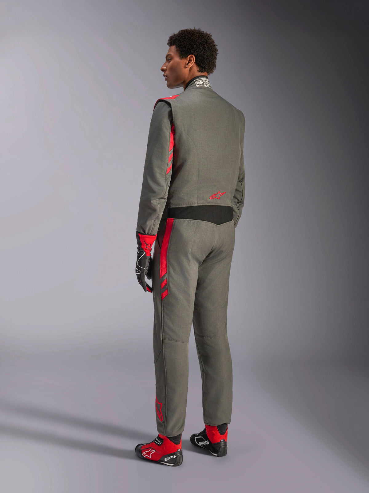 Alpinestars GP Race V3 Suit FIA, mono de carreras Anthracite Red, vista posterior del modelo con el traje de dos capas, detalles rojos en hombros y piernas, combinado con guantes y botas a juego, equipamiento profesional para automovilismo