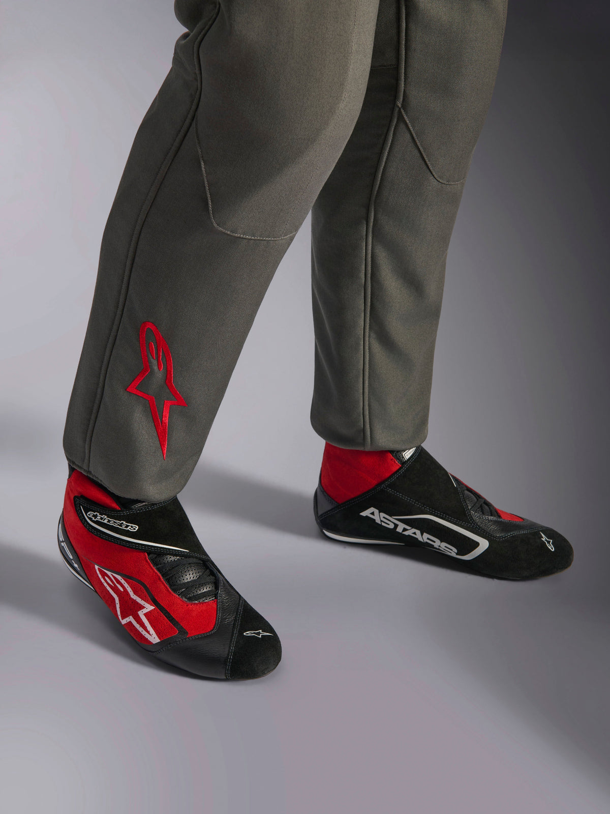Alpinestars Mono GP Race V3 FIA, traje de carreras Antracita Rojo, primer plano de las piernas con el logotipo de la estrella roja bordado, combinado con botas de carreras rojas y negras, equipo profesional de automovilismo diseñado para la protección y comodidad del piloto