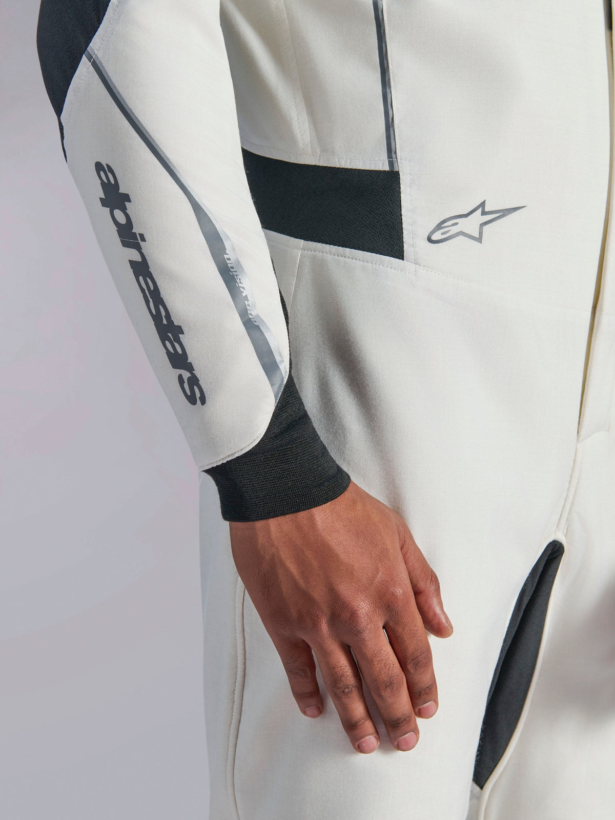 Alpinestars Hypertech V3 Suit, primer plano de un mono de automovilismo blanco con detalles en negro y plateado, logotipo de Alpinestars en el antebrazo, puño de punto negro y paneles elásticos oscuros para mayor movilidad, equipamiento profesional para deportes de motor