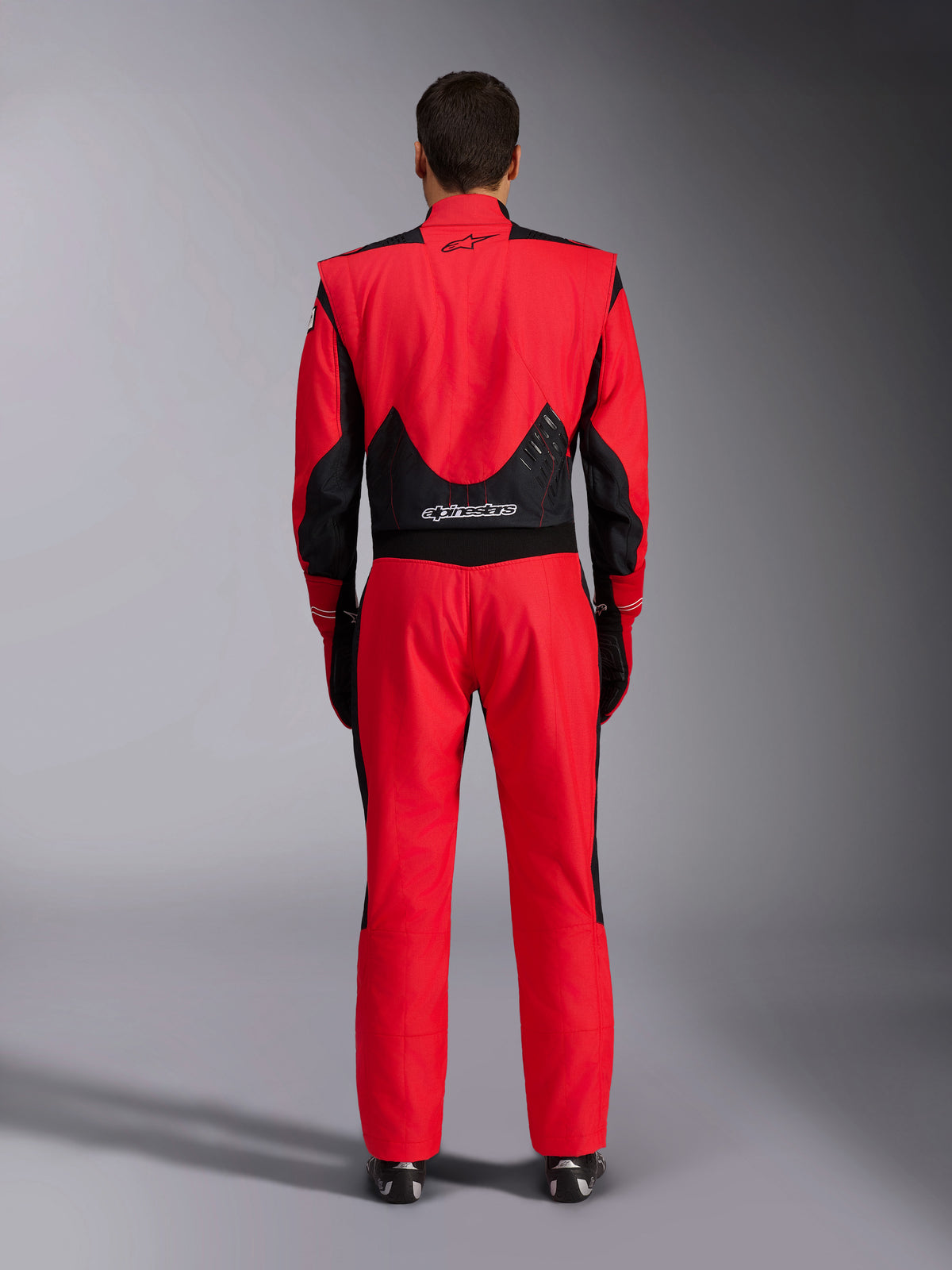 Traje de carreras Alpinestars GP Pro Comp V2 FIA, rojo y negro, vista posterior que muestra paneles de malla negra y elásticos en la parte inferior de la espalda, logotipo de Alpinestars en la zona superior e inferior de la espalda, equipamiento profesional para automovilismo