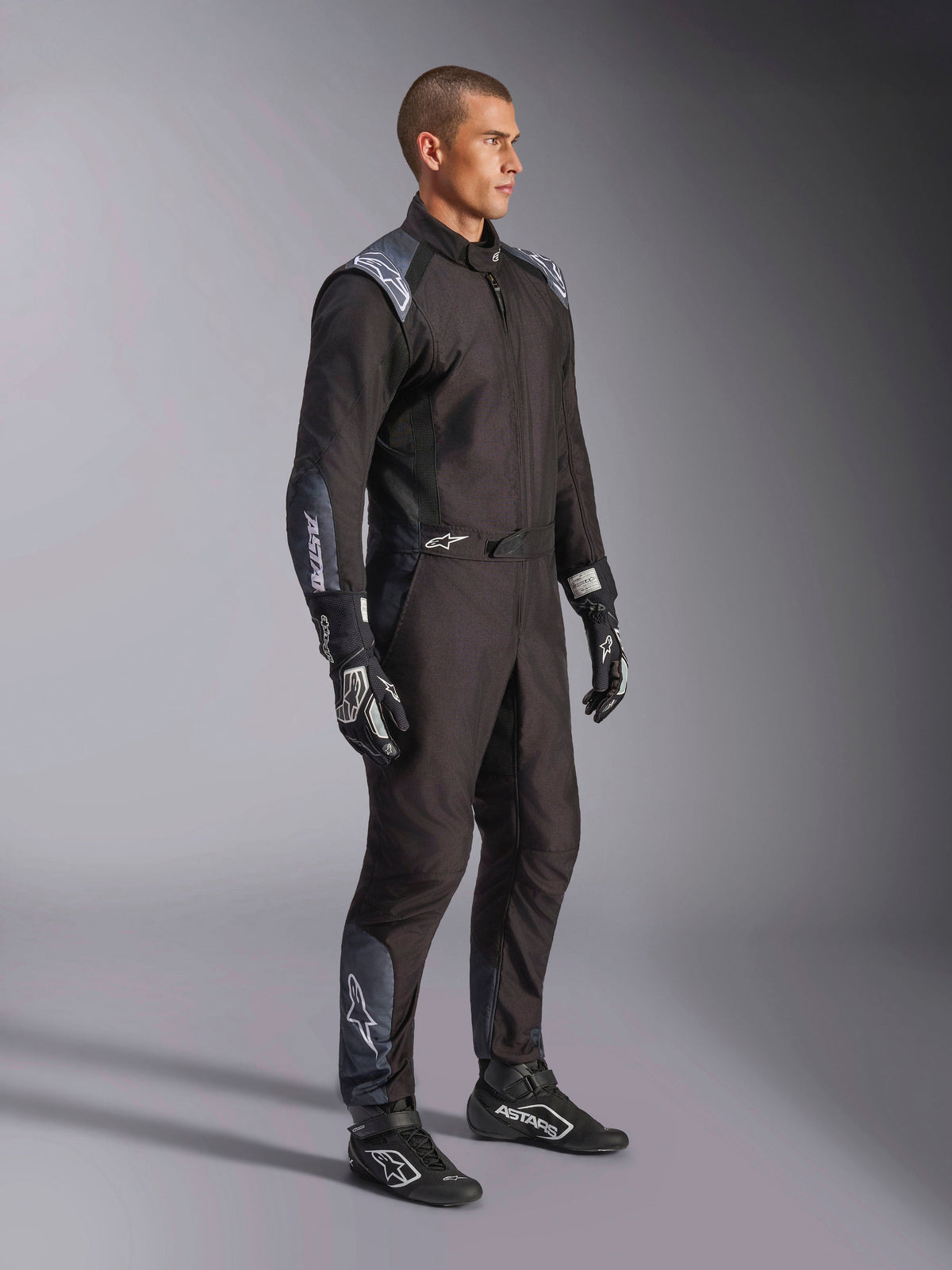 Traje Alpinestars KMX-5 V3, mono de karting en Black Dark Shadow, usado con guantes y calzado de carreras negros a juego, con perforaciones cortadas a láser y paneles de malla técnica, elegante diseño de doble capa con logotipos en blanco para automovilismo profesional.